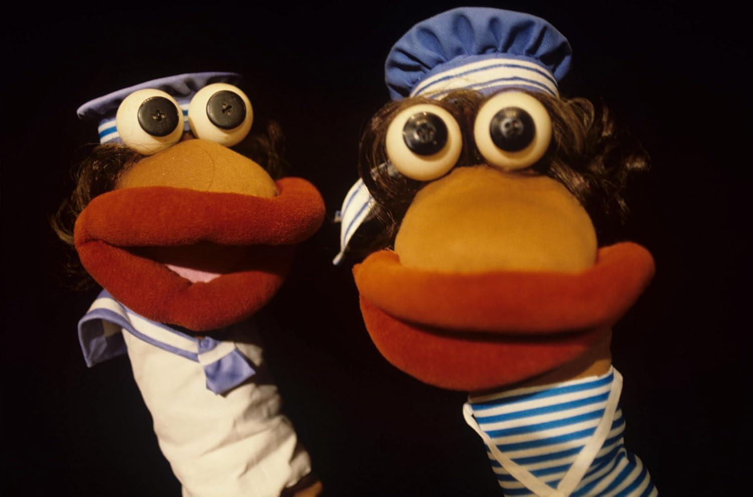 Zwei Sockenpuppen mit großen Lippen und Augen. Sie tragen Matrosenmützen und gestreifte Hemden.