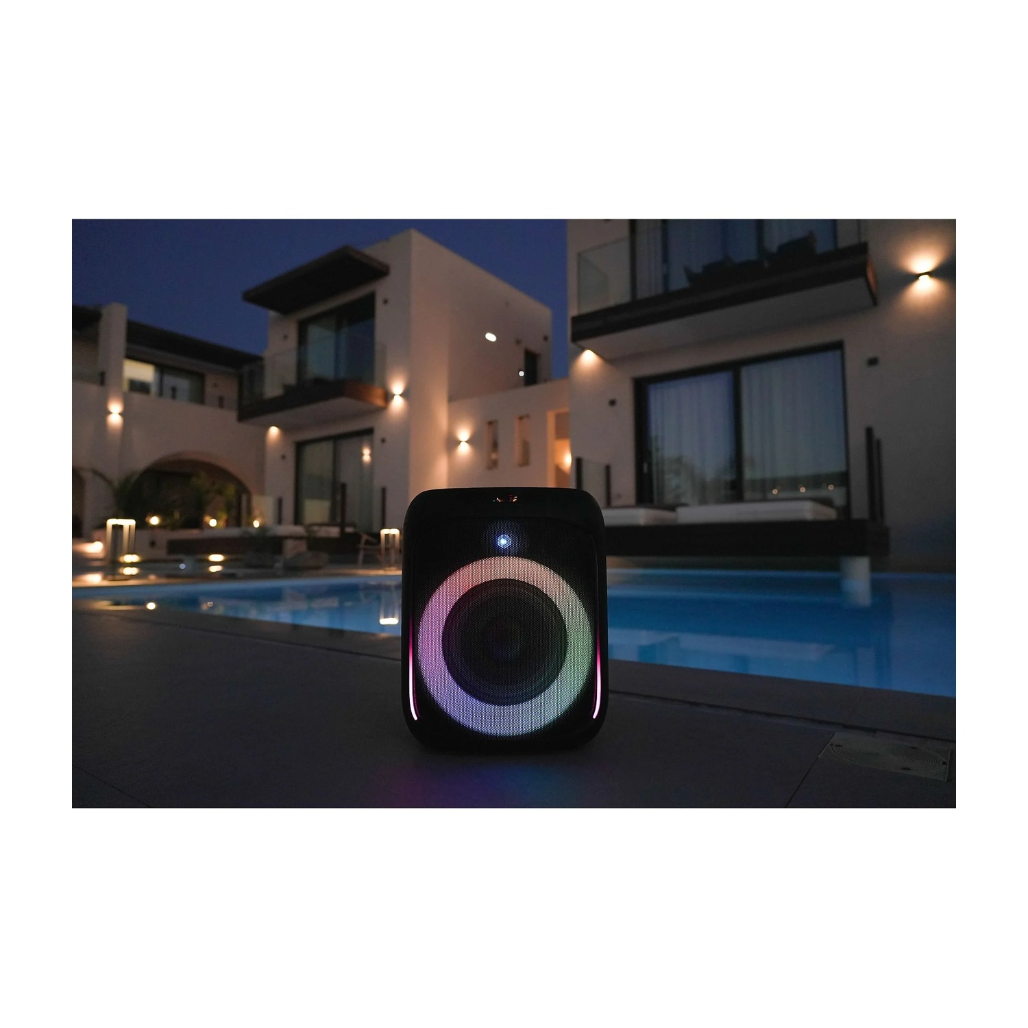Diffusore nero con anello luminoso colorato a bordo piscina di notte. Case e luci sullo sfondo.