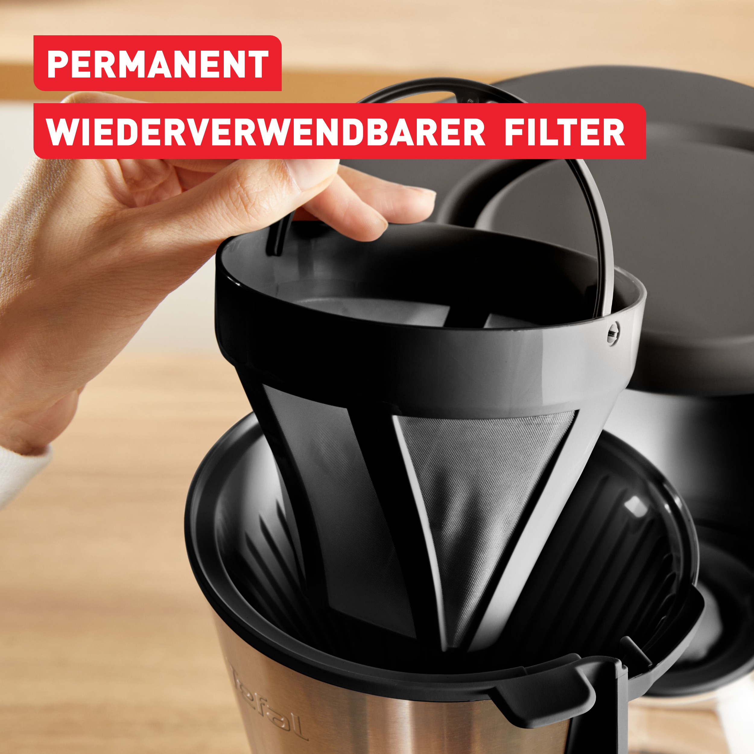 Eine Hand hält einen wiederverwendbaren schwarzen Kaffeefilter aus einer Kaffeemaschine. Roter Text sagt permanent, wiederverwendbarer Filter.
