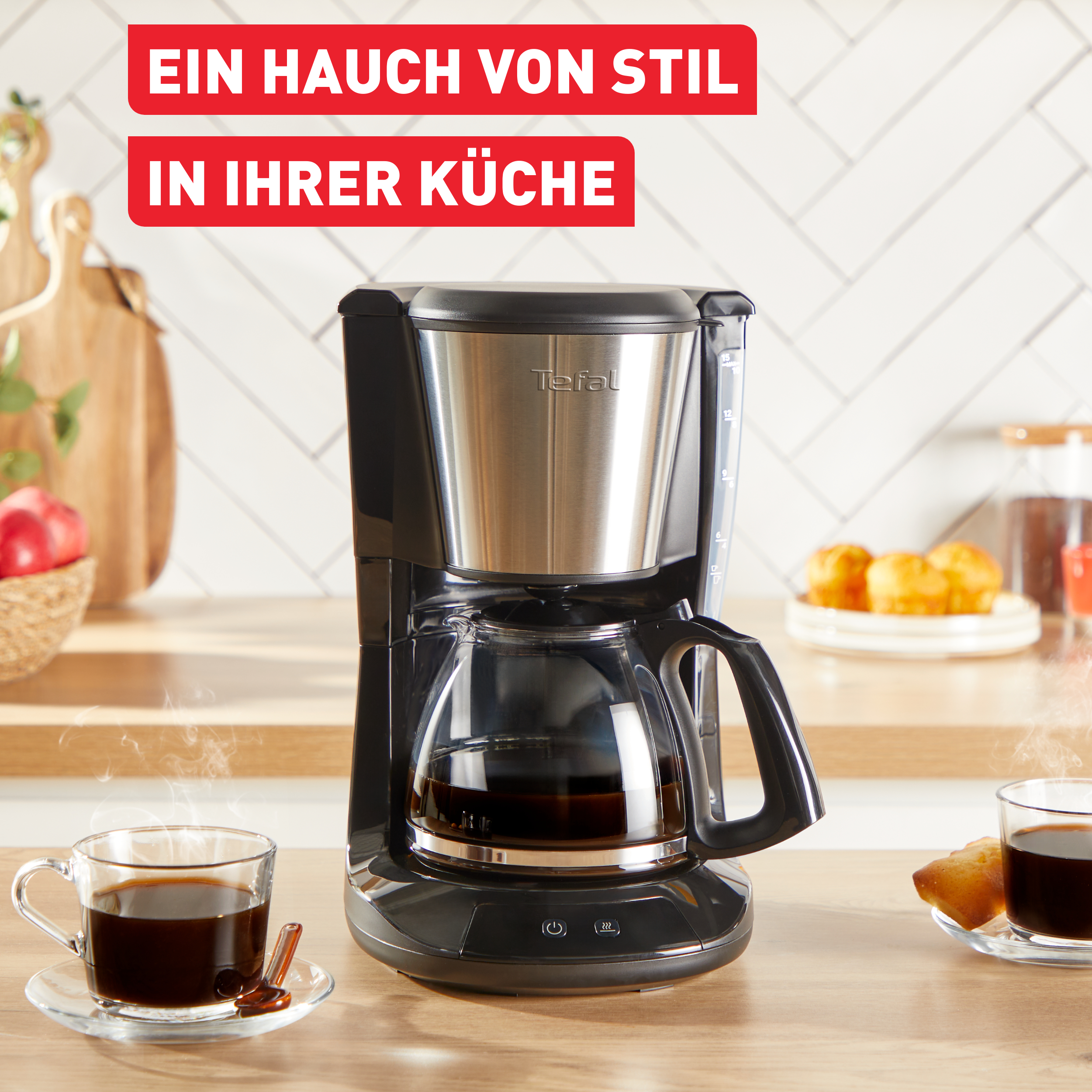 Schwarze Kaffeemaschine mit Glaskaraffe, Dampf und zwei Kaffeetassen auf Holzoberfläche.