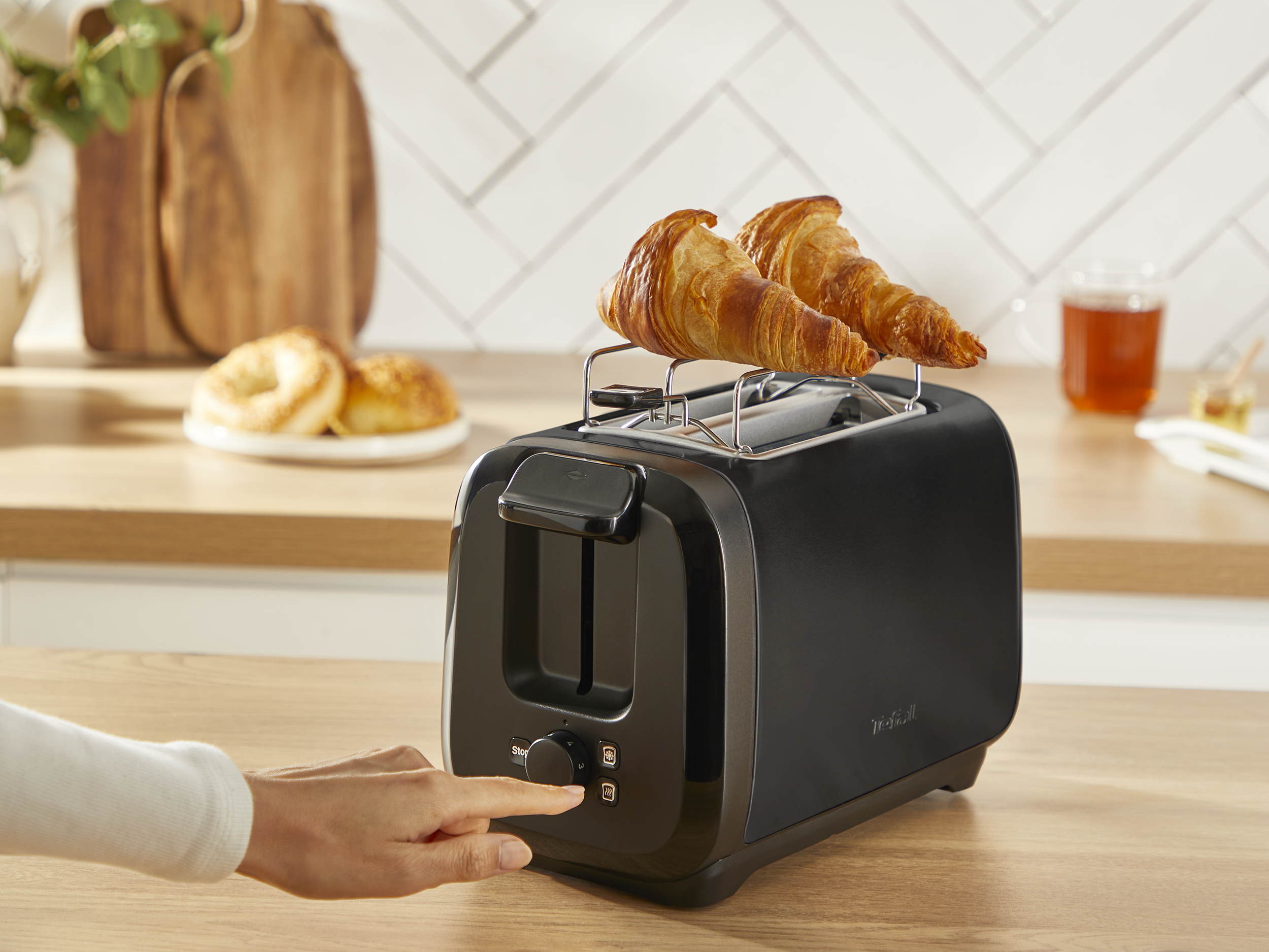 Fekete kenyérpirító croissant-okkal. A kéz a gombra mutat.