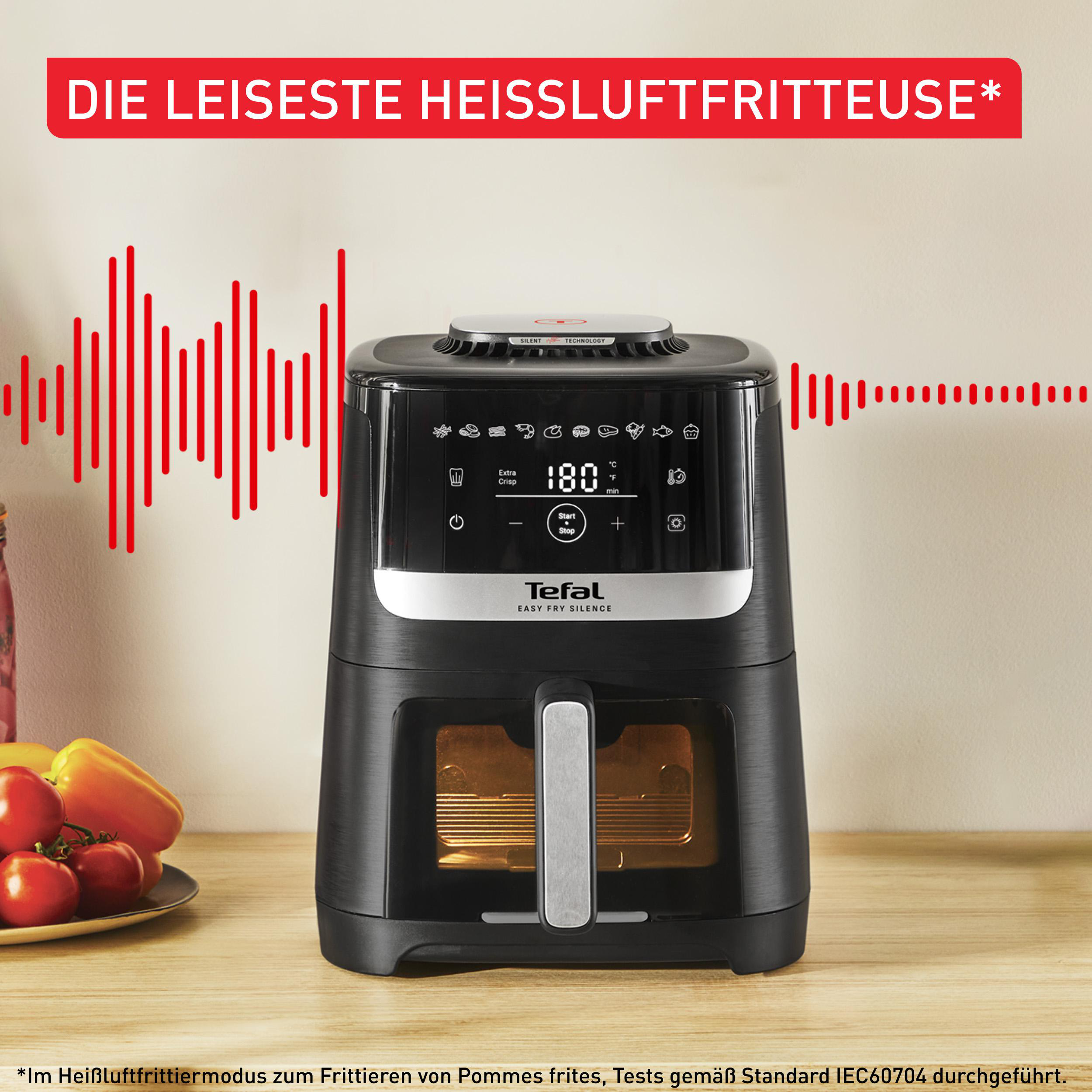 Schwarze Heißluftfritteuse. Text: 'Die leiseste Heißluftfritteuse'. Schallwellen. Tomaten und Paprika.