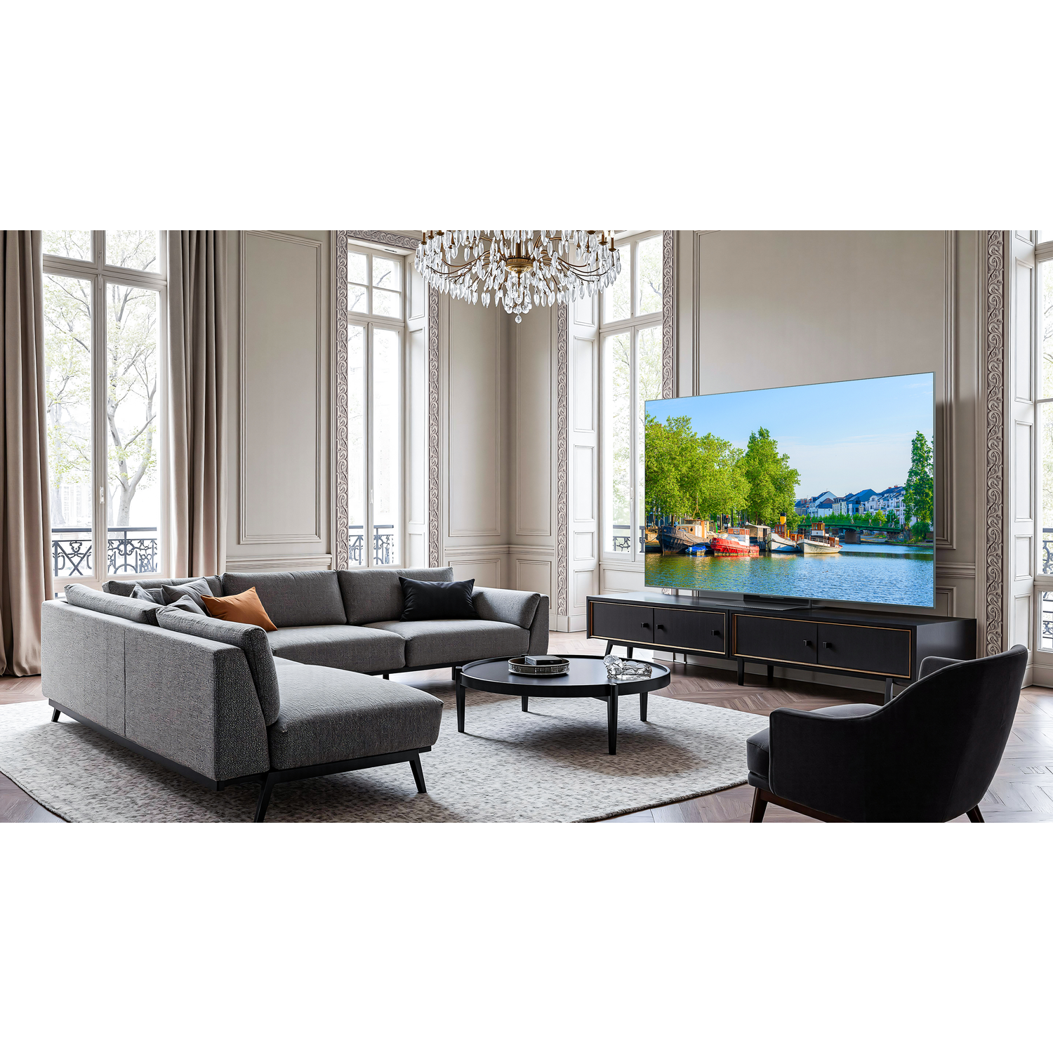 Een woonkamer met een TCL tv die een rivierlandschap toont. Met een grijze bank, een zwarte tafel en een kroonluchter.