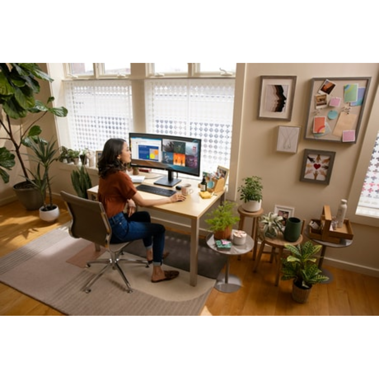 Vrouw werkt op gebogen HP-monitor aan een bureau, planten en decoratie op de achtergrond.