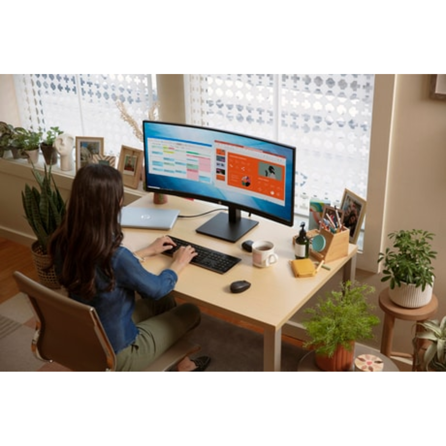 Vrouw werkt op gebogen HP-monitor. Toetsenbord, muis, beker en planten op bureau.