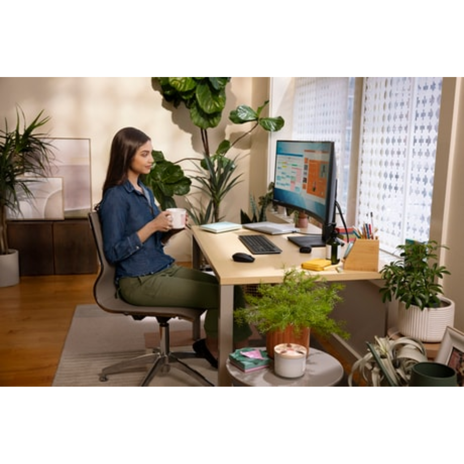 Vrouw houdt een kopje vast, kijkt naar gebogen HP-monitor, planten en bureau.