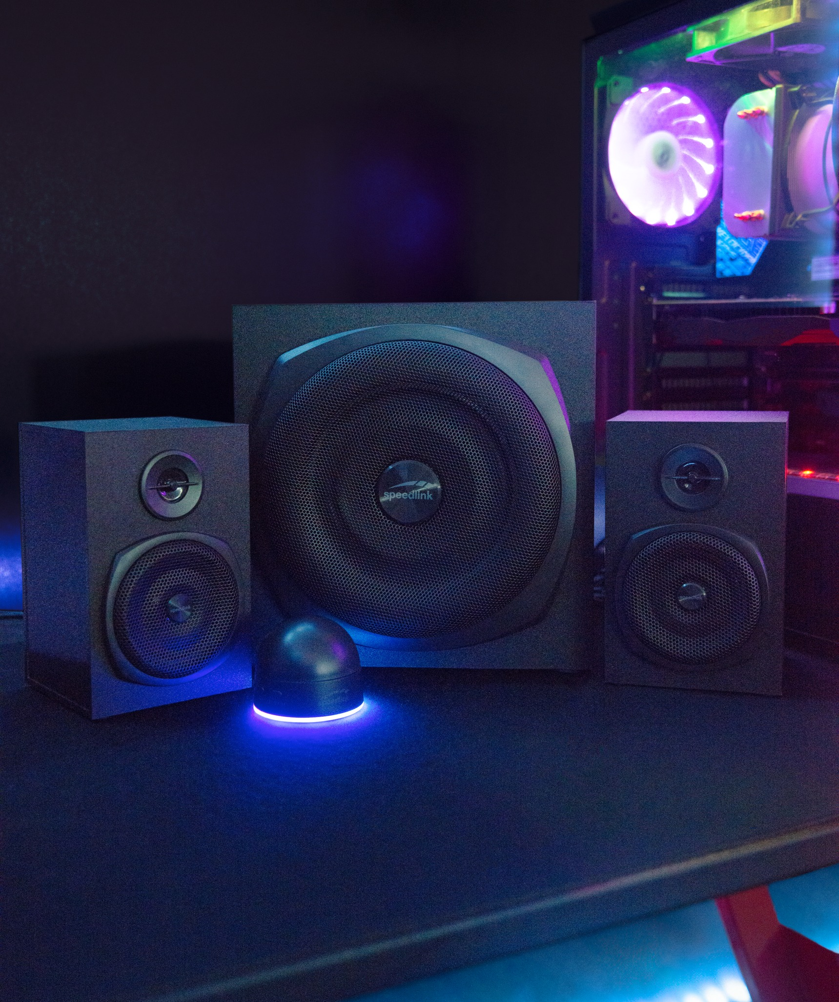Schwarzes Lautsprechersystem in einem Gaming-Setup. Subwoofer, Lautsprecher, Control Pod und Computer sichtbar.