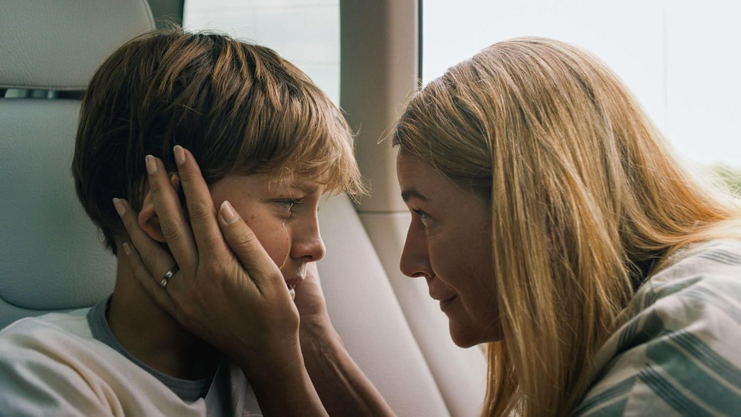 Mutter und Sohn stehen sich gegenüber, Hände auf seinem Gesicht im Auto.