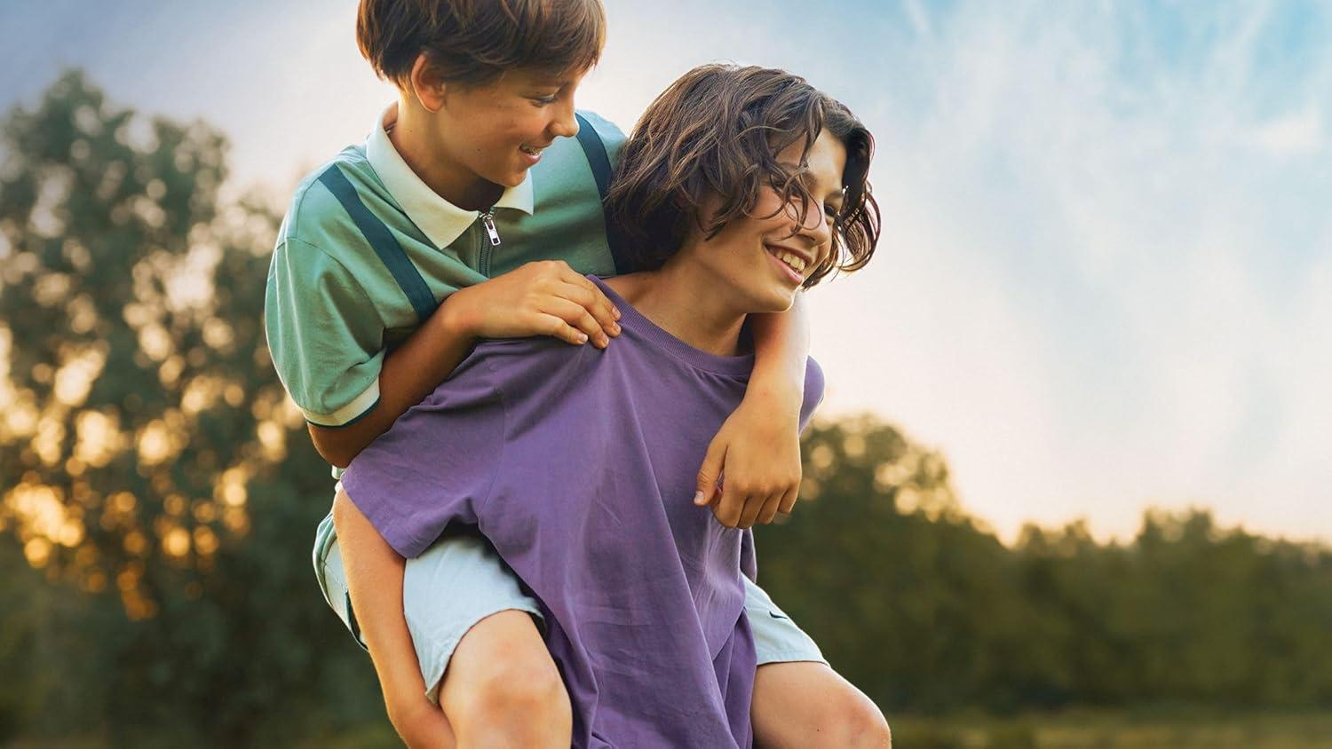 Zwei Jungen lächeln, einer trägt den anderen auf dem Rücken auf einem Feld.