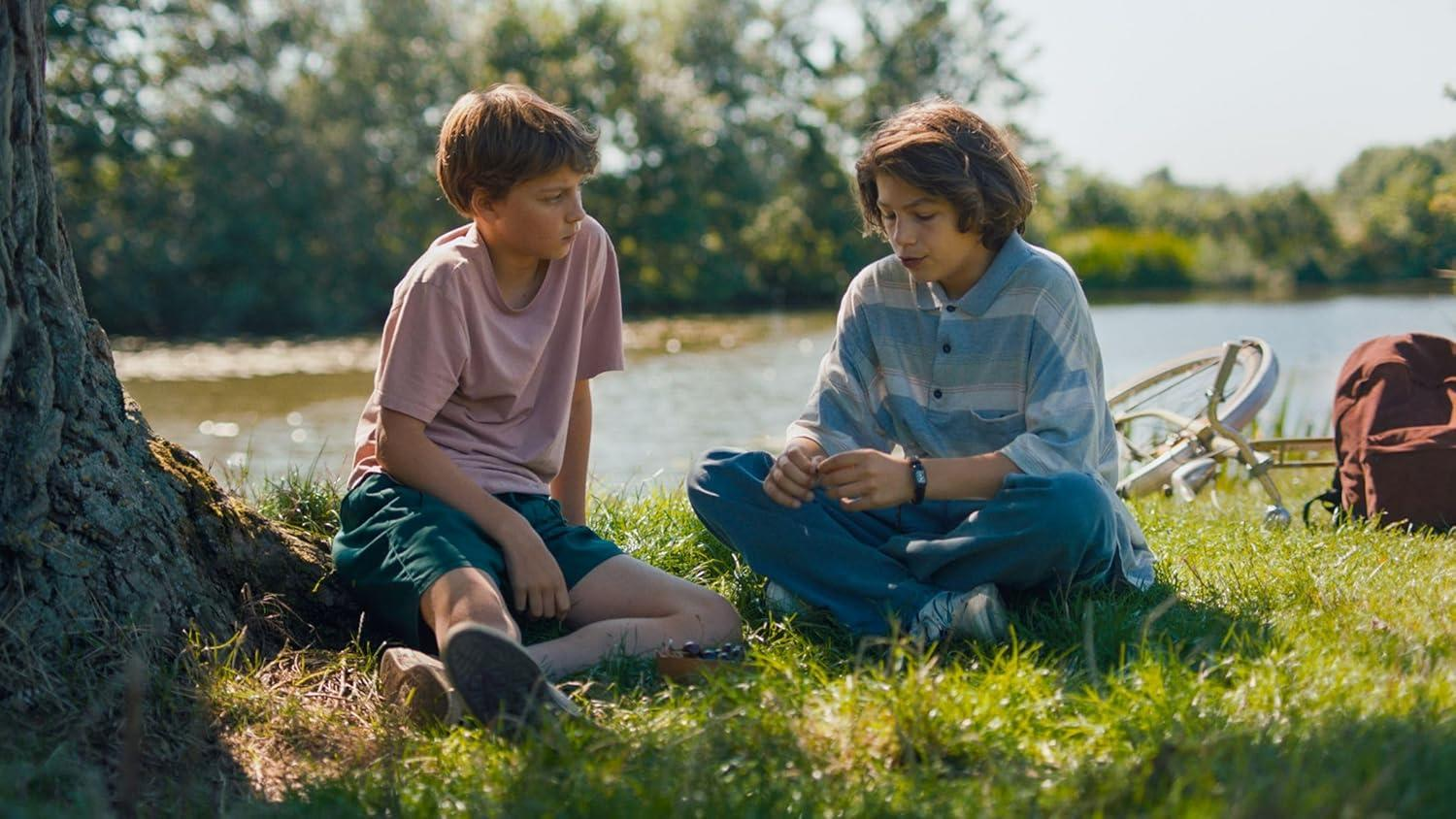 Zwei Jungen sitzen auf Gras, reden in der Nähe eines Sees mit Fahrrad.