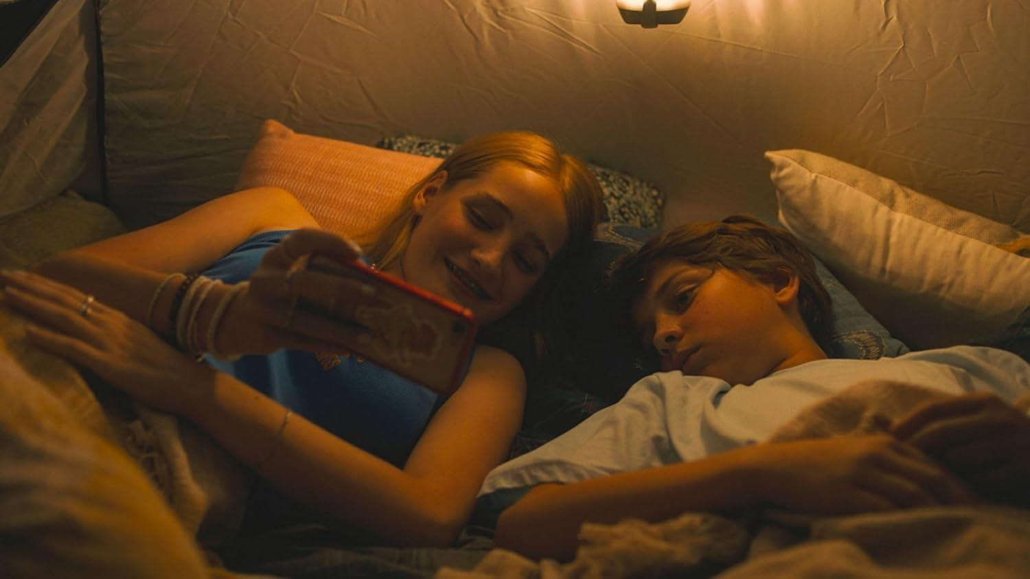 Zwei Personen in einem Zelt, eine hält ein Telefon, die andere ruht.