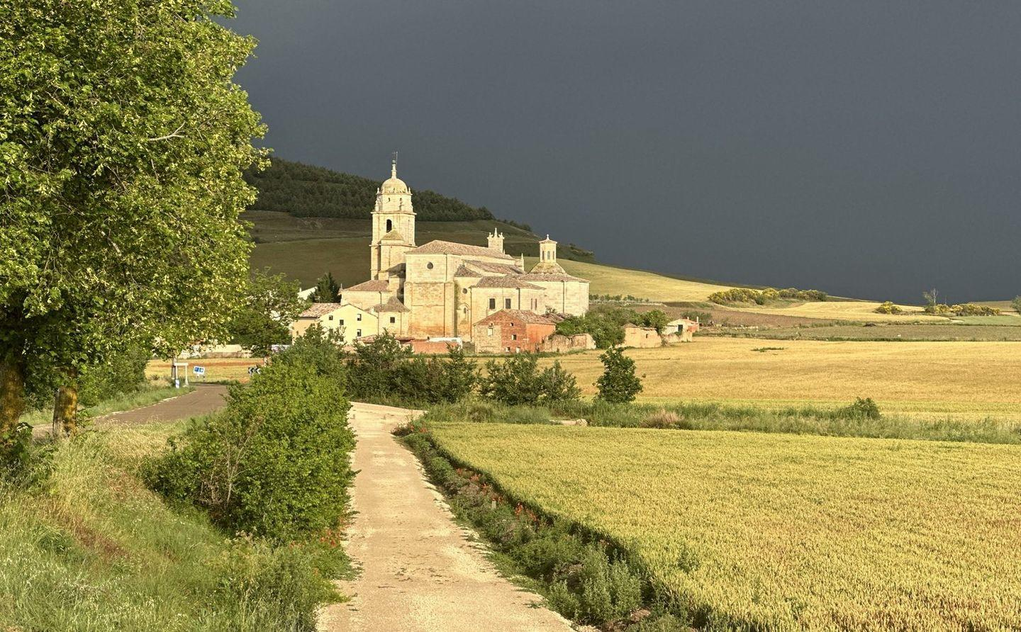 Eine Kirche mit dunklem Himmel. Eine Straße führt über ein Feld zur Kirche.