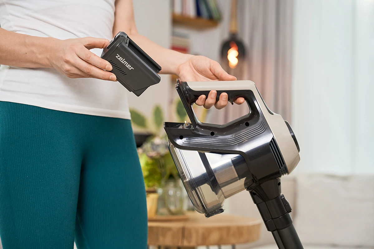 Osoba trzymająca baterię i odkurzacz. Scena w pomieszczeniu.