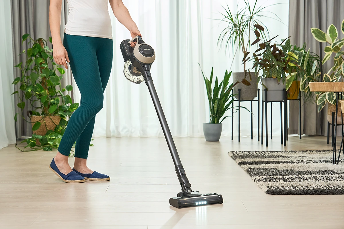 Kobieta odkurza drewnianą podłogę w domu.