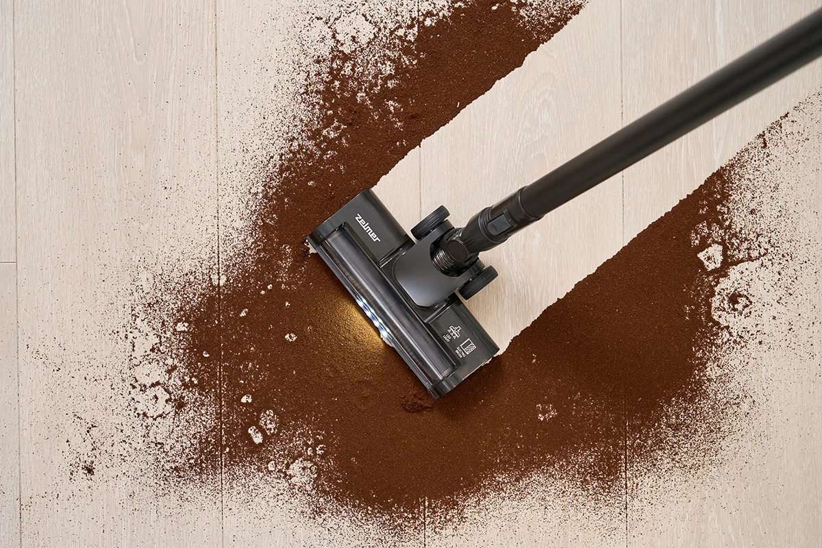 Odkurzacz czyszczący drewnianą podłogę pokrytą fusami z kawy.