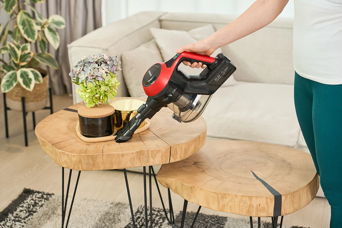 Kobieta trzyma czerwony odkurzacz nad stołami, blisko kwiatów i dekoracji, w pomieszczeniu, w legginsach.