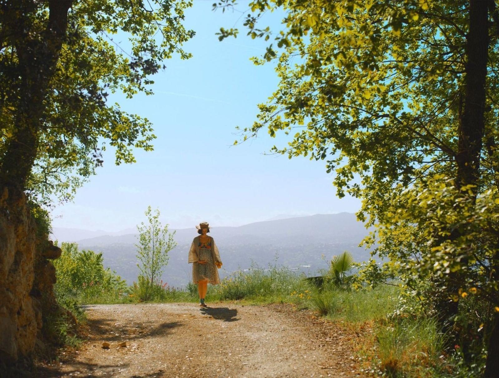 Eine Frau geht auf einem Weg, umgeben von Bäumen, auf eine malerische Aussicht zu.