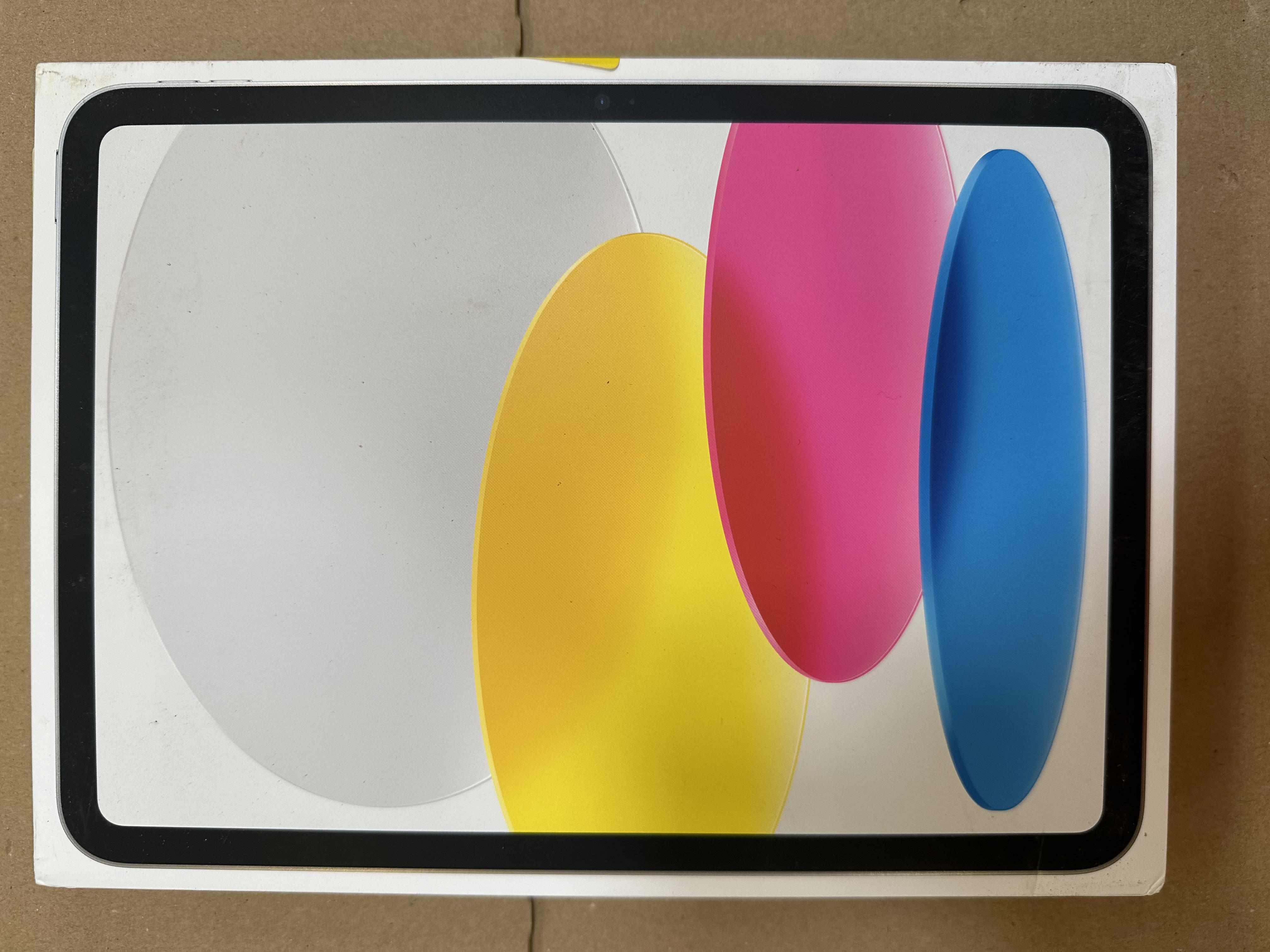 Pudełko tabletu z abstrakcyjnym wzorem. Białe tło z żółtymi, różowymi i niebieskimi kształtami. Czarne obramowanie.