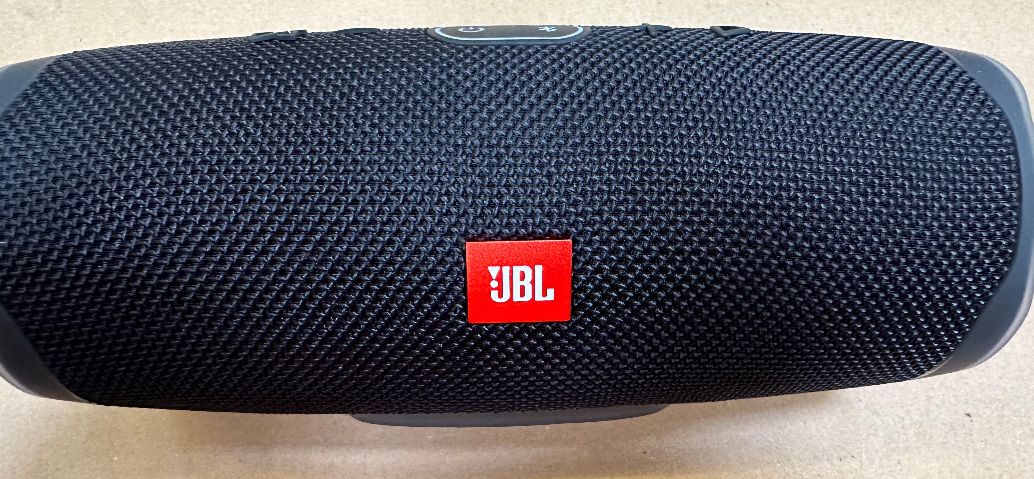 Czarny głośnik JBL Charge 4. Logo JBL na czerwonym kwadracie pośrodku. Widoczna faktura materiału.