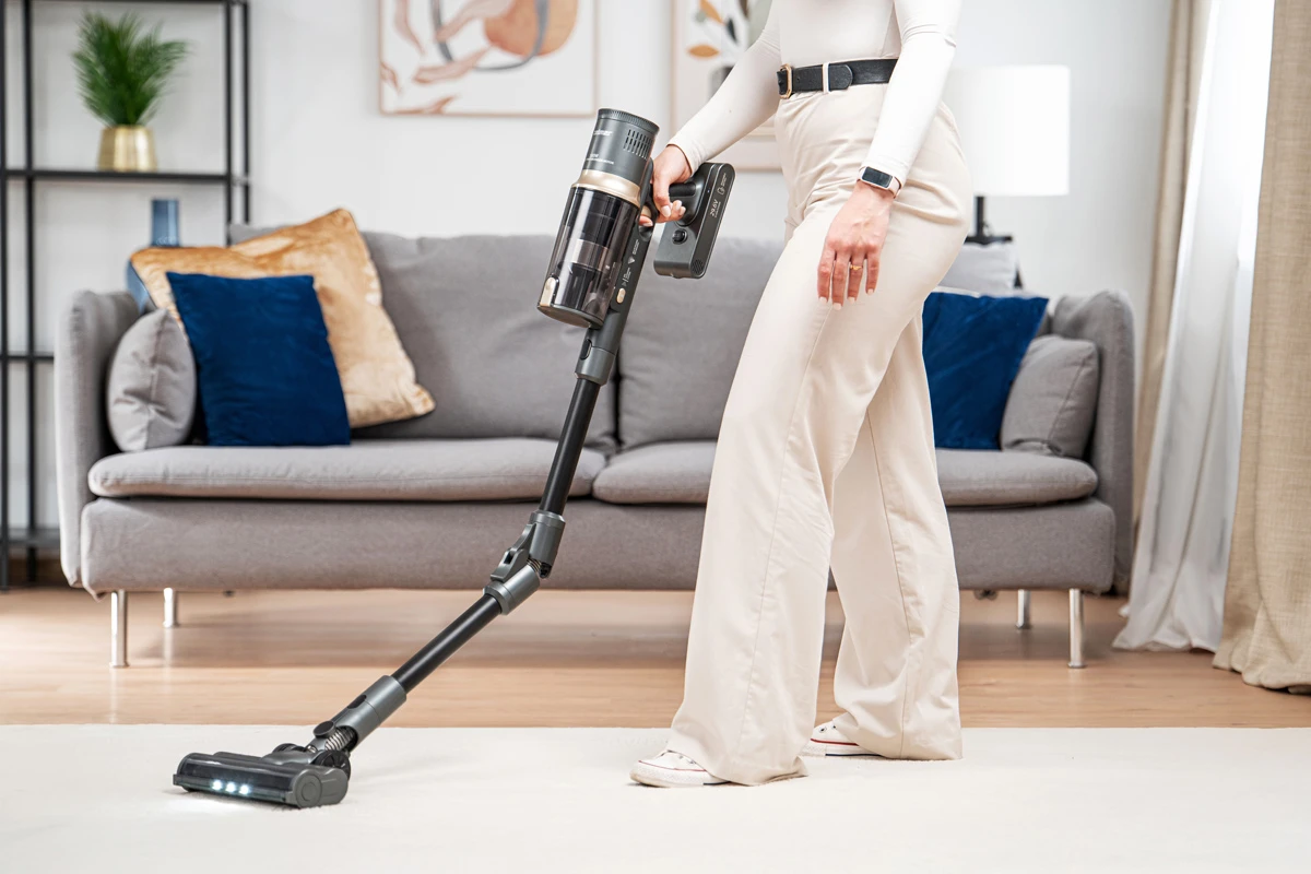 Osoba używająca odkurzacza bezprzewodowego na dywanie w salonie.