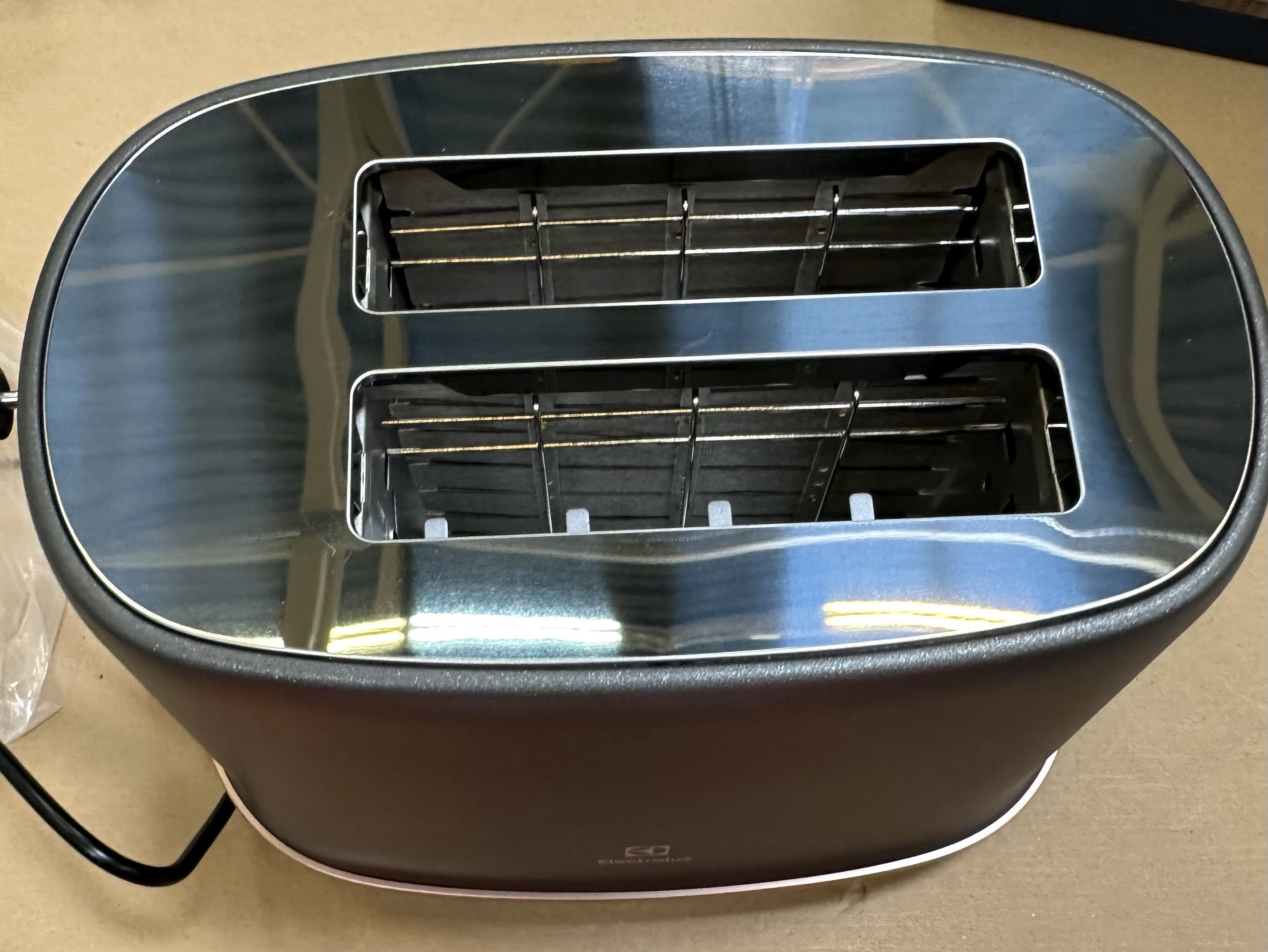 Widok z góry na czarny toster Electrolux z dwoma otworami. Wnętrze wykonane jest ze stali nierdzewnej. Toster stoi na jasnobrązowej powierzchni.