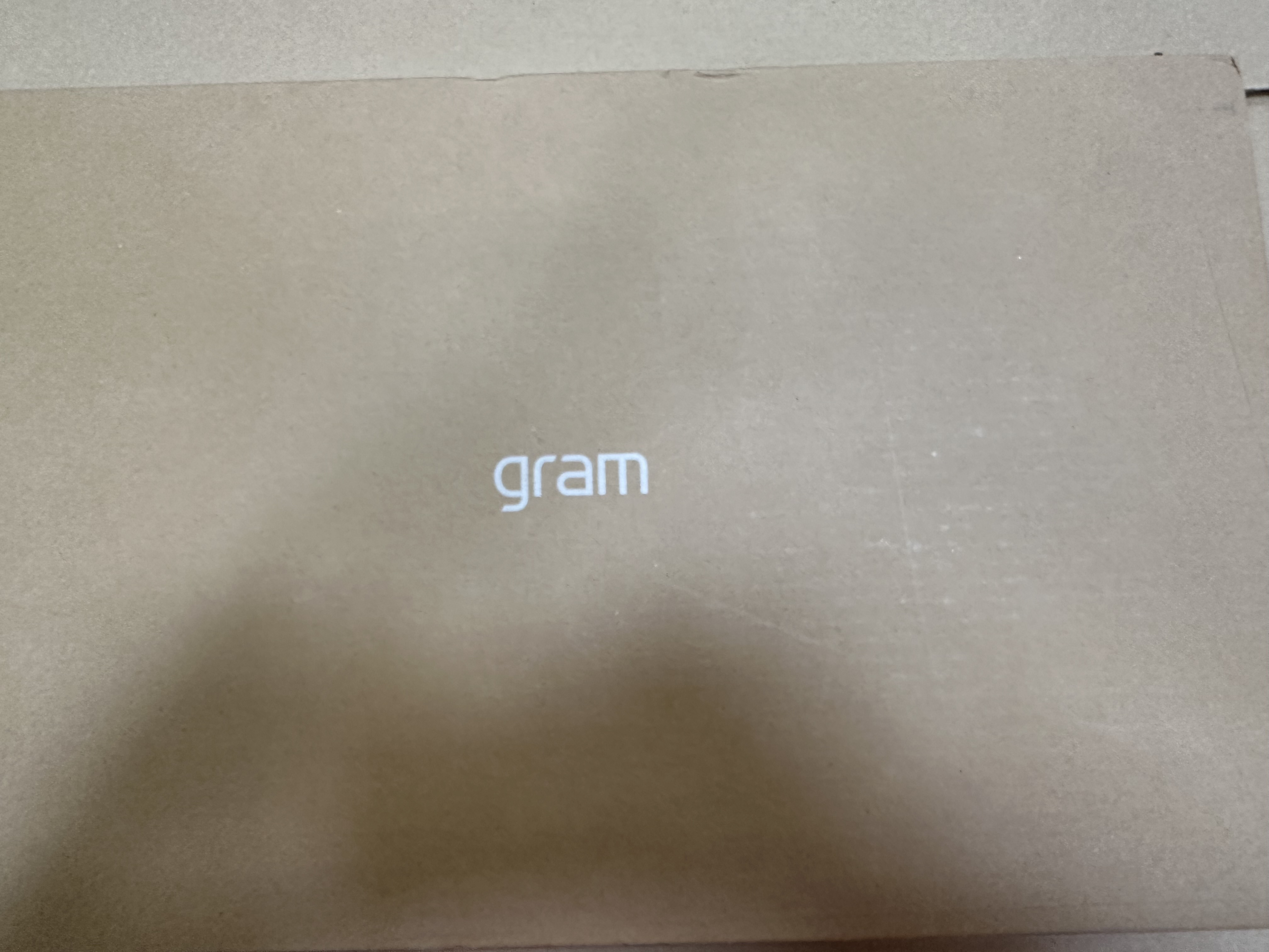 Kartonowe pudełko z napisem "gram" w białym tekście. Pudełko jest gładkie brązowe. Powierzchnia jest lekko zużyta.