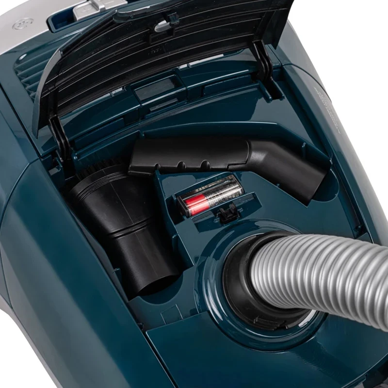 Otwarta komora turkusowego odkurzacza, ujawniająca wąż i schowek na akcesoria.