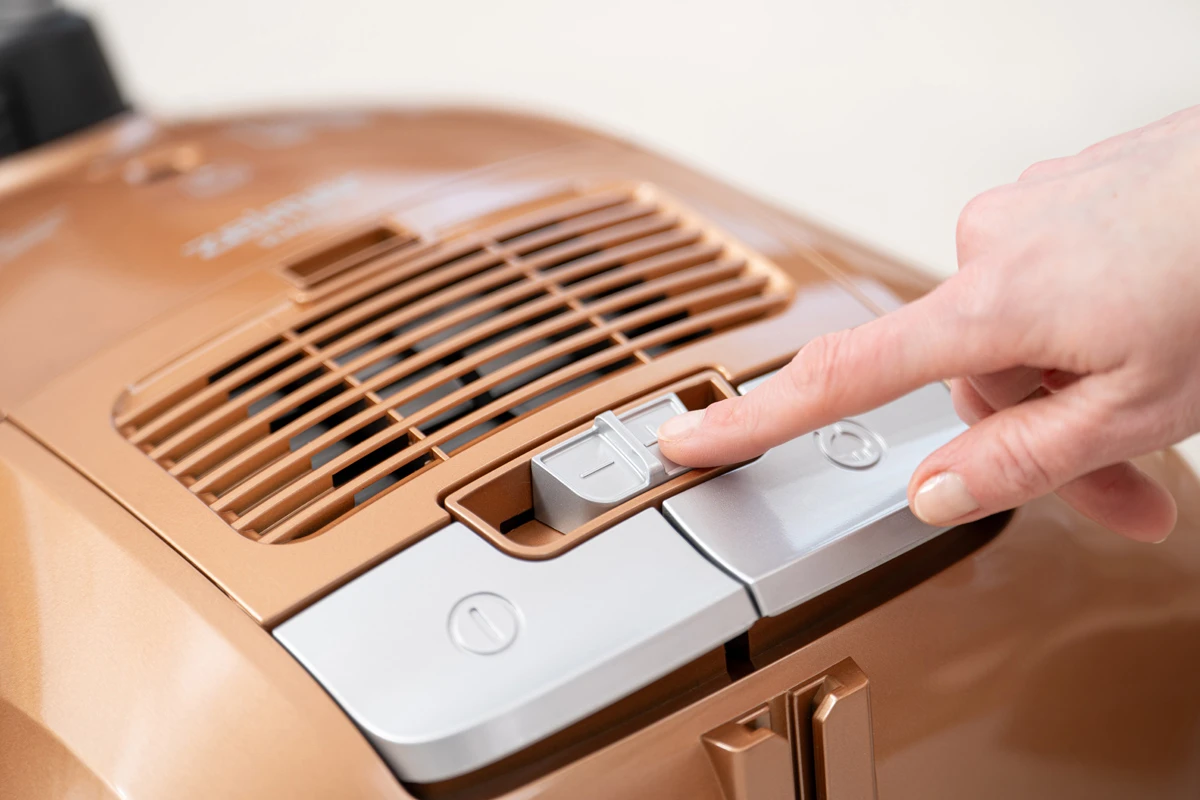 Ręka osoby naciskająca przycisk na złotym odkurzaczu.