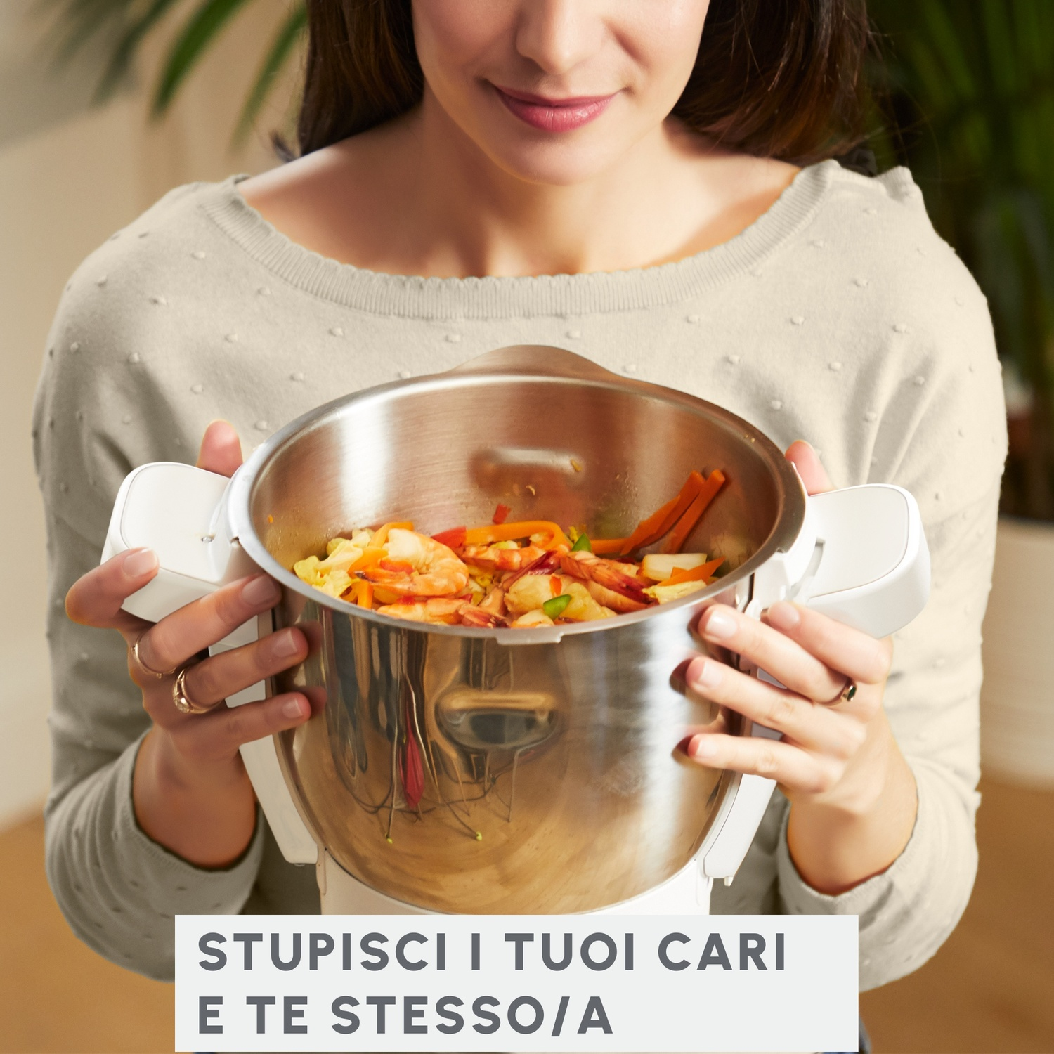 Una donna tiene in mano un elettrodomestico bianco con una ciotola di cibo. Sorride. Testo: 'Sorprendi i tuoi cari'.