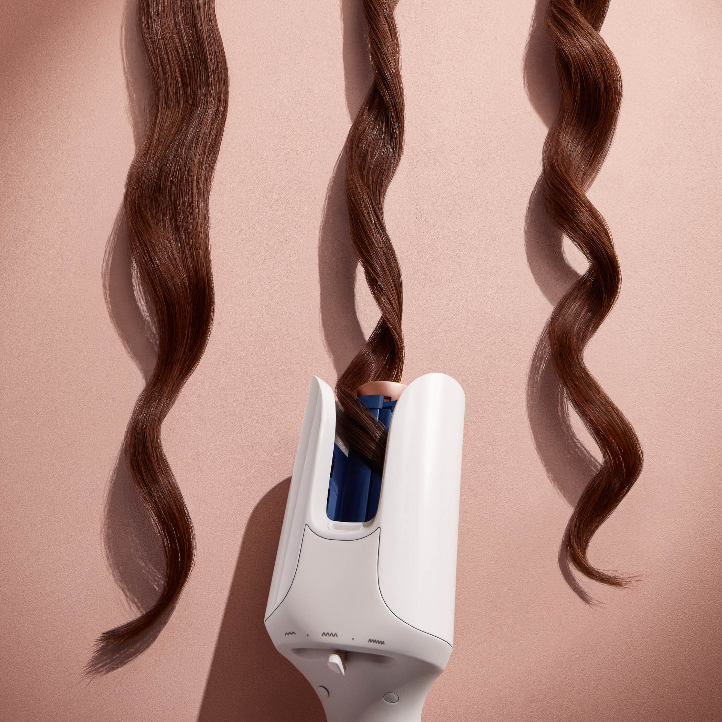 Lokówka z trzema pasmami brązowych włosów. Lokówka jest pośrodku, kręci włosy.