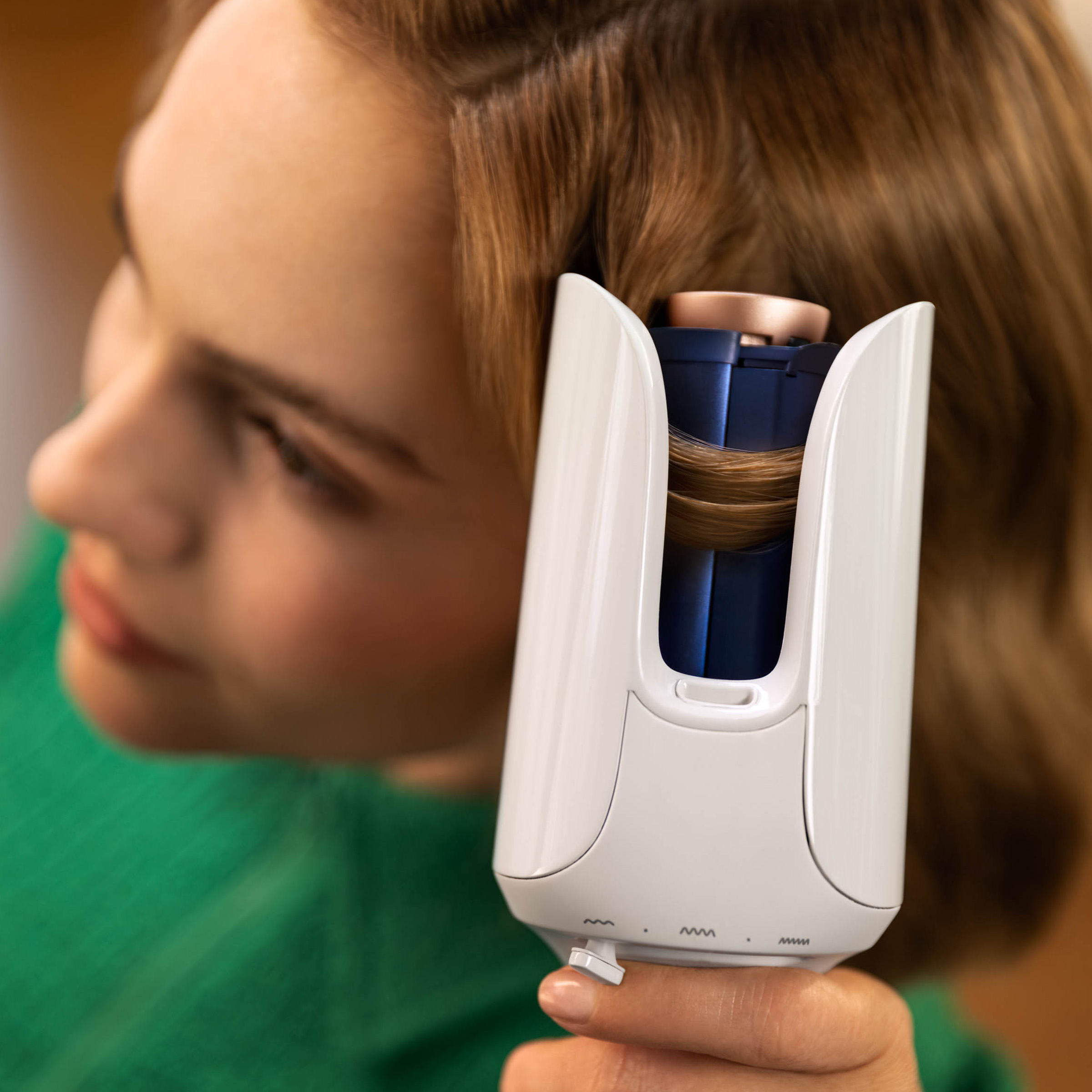 Kobieta używa lokówki na swoich włosach. Lokówka jest biała, z włosami wokół niej.