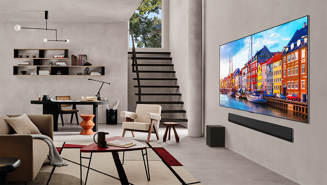 Nappali nagy TV-vel, színes vízparti jelenettel, soundbarral és kényelmes ülősarokkal.