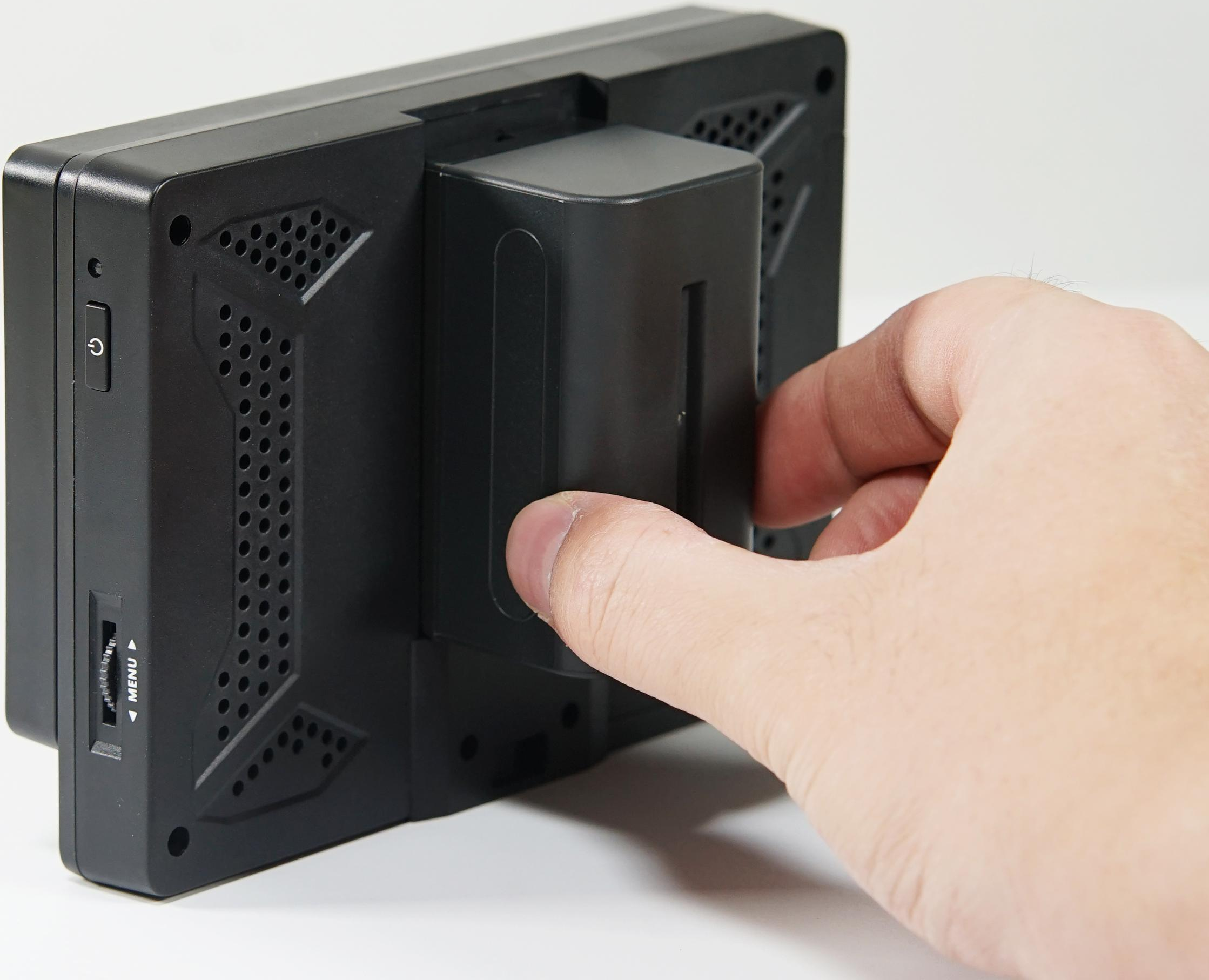 La main insère une batterie dans un moniteur vidéo noir. Fond blanc.