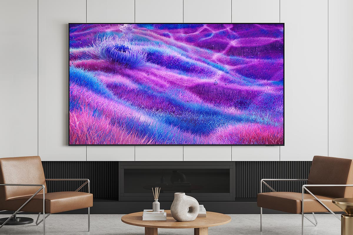 TV a parete mostra un'opera d'arte astratta viola e blu. Due sedie marroni davanti a un camino.