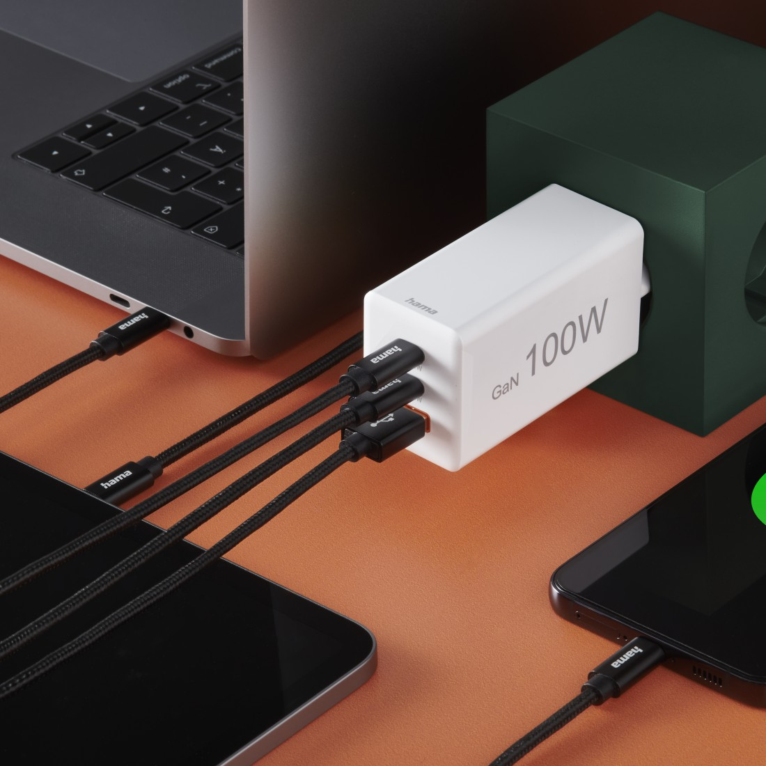 Ladegerät versorgt Laptop, Tablet und Telefon mit schwarzen Kabeln.