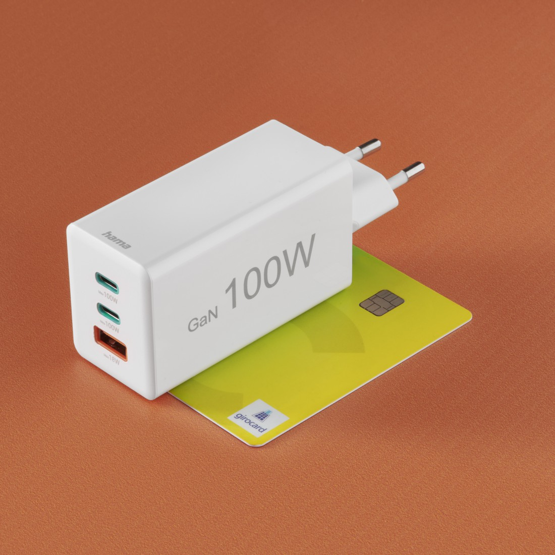 Weißes GaN 100W Ladegerät auf einer grün-gelben Kreditkarte. Der Hintergrund ist orange.