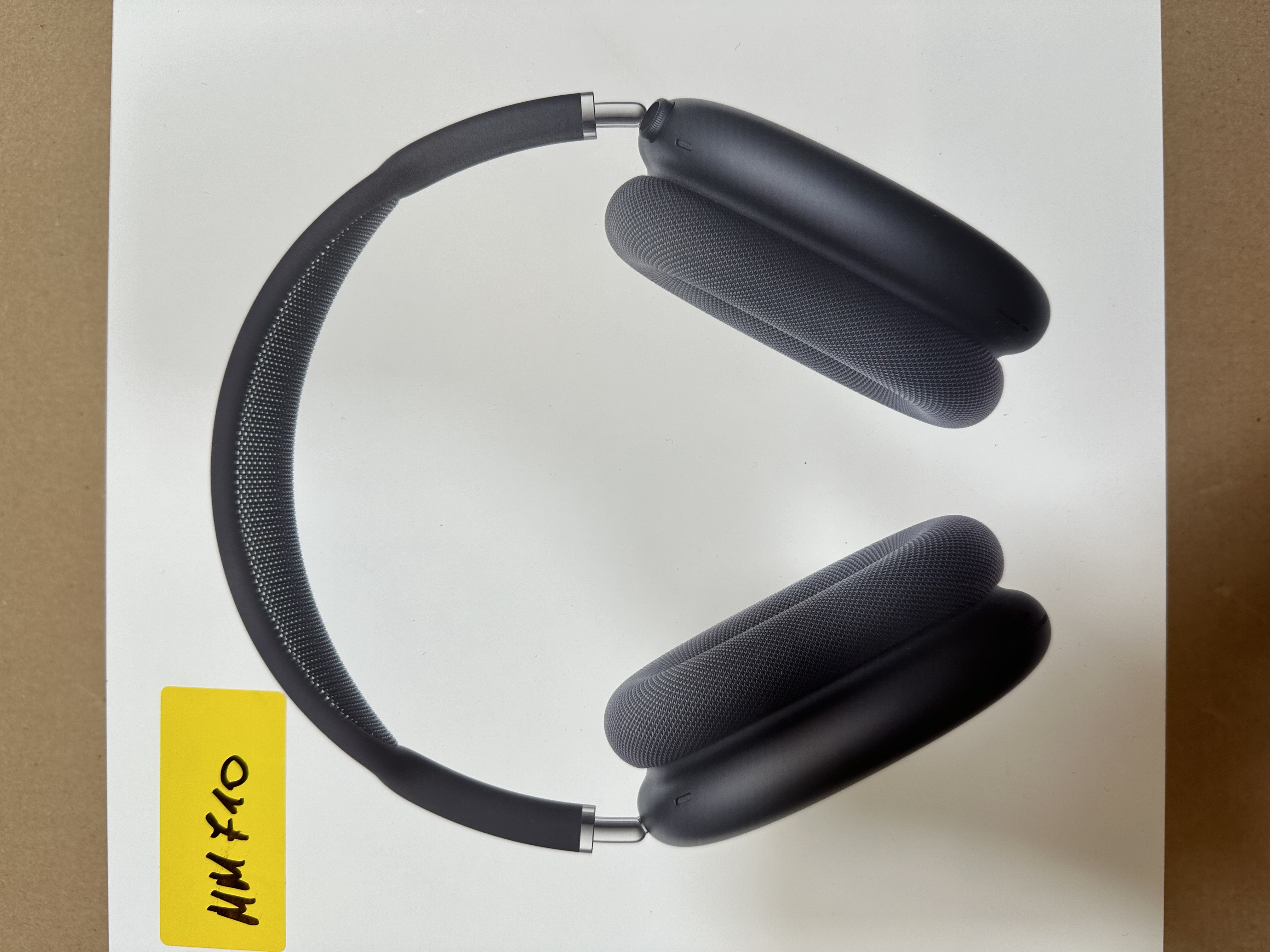Czarne słuchawki Apple AirPods Max na białym pudełku. Żółta naklejka z tekstem znajduje się na pudełku.