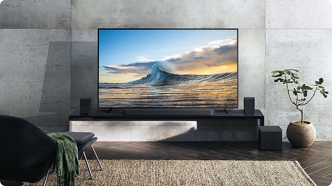 Salon avec TV, barre de son, enceintes et tapis. La TV affiche une vague sur la plage.