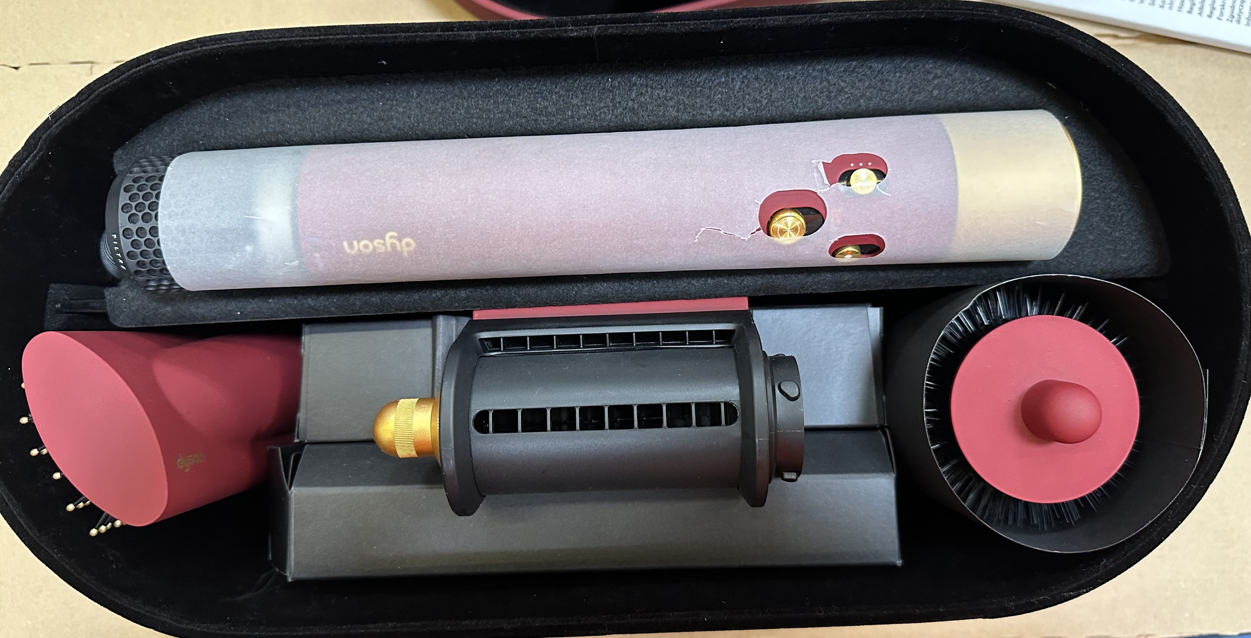 Elementy stylizatora do włosów Dyson w czarnej walizce: lufa, nasadki i jednostka główna, wszystko w kolorze czerwono-czarnym.