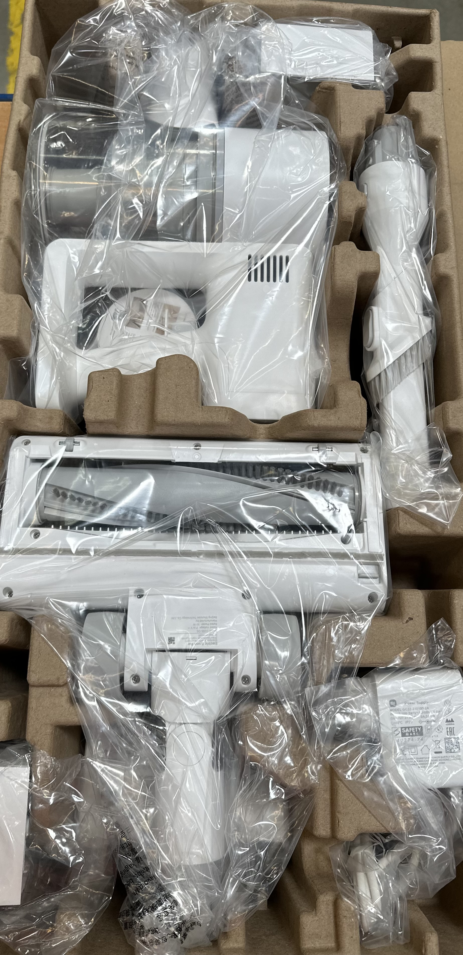 Biały odkurzacz i akcesoria, zapakowane w plastik i tekturę.