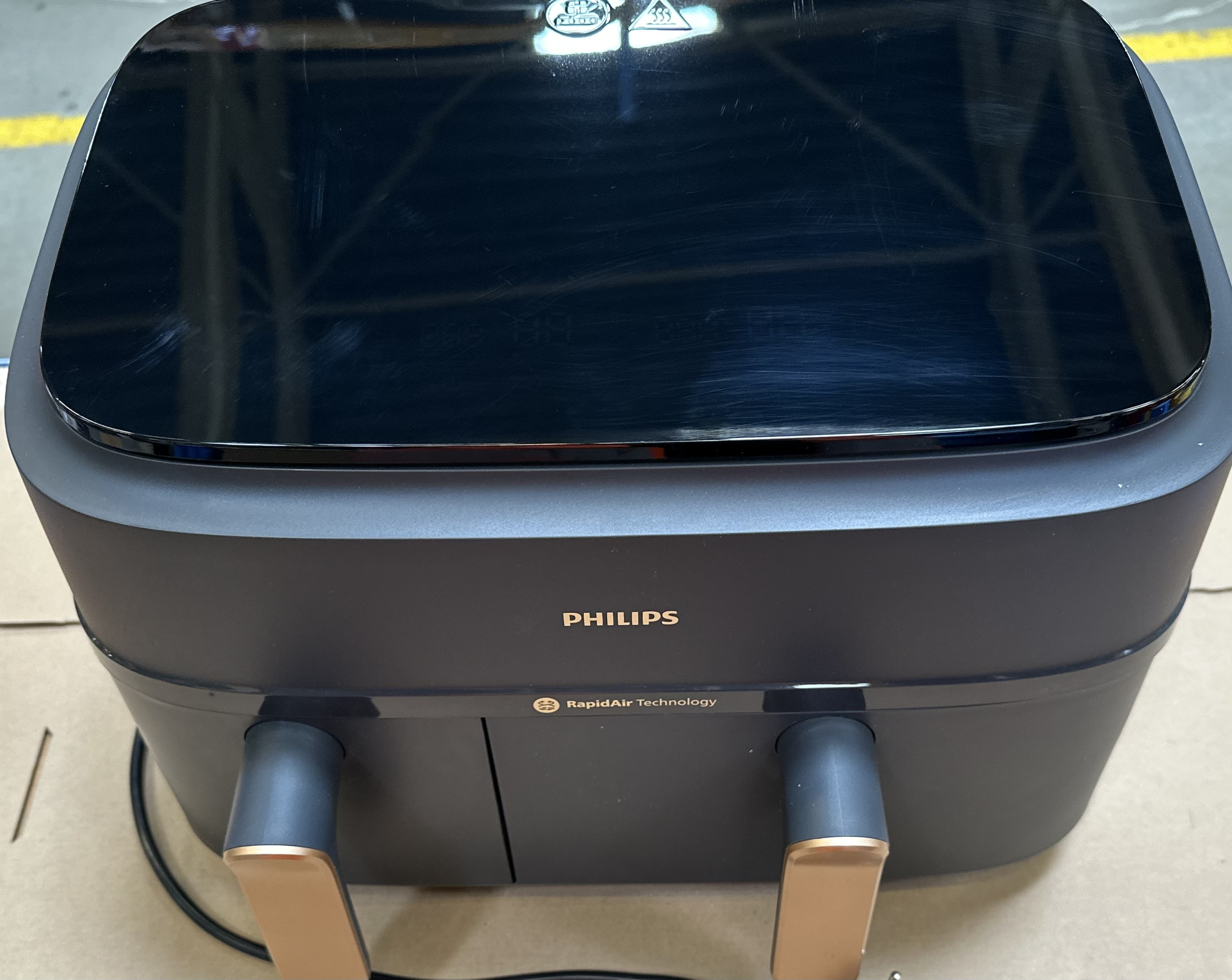 Frytkownica powietrzna, czarna z błyszczącym blatem. Złote uchwyty i widoczne logo Philips.