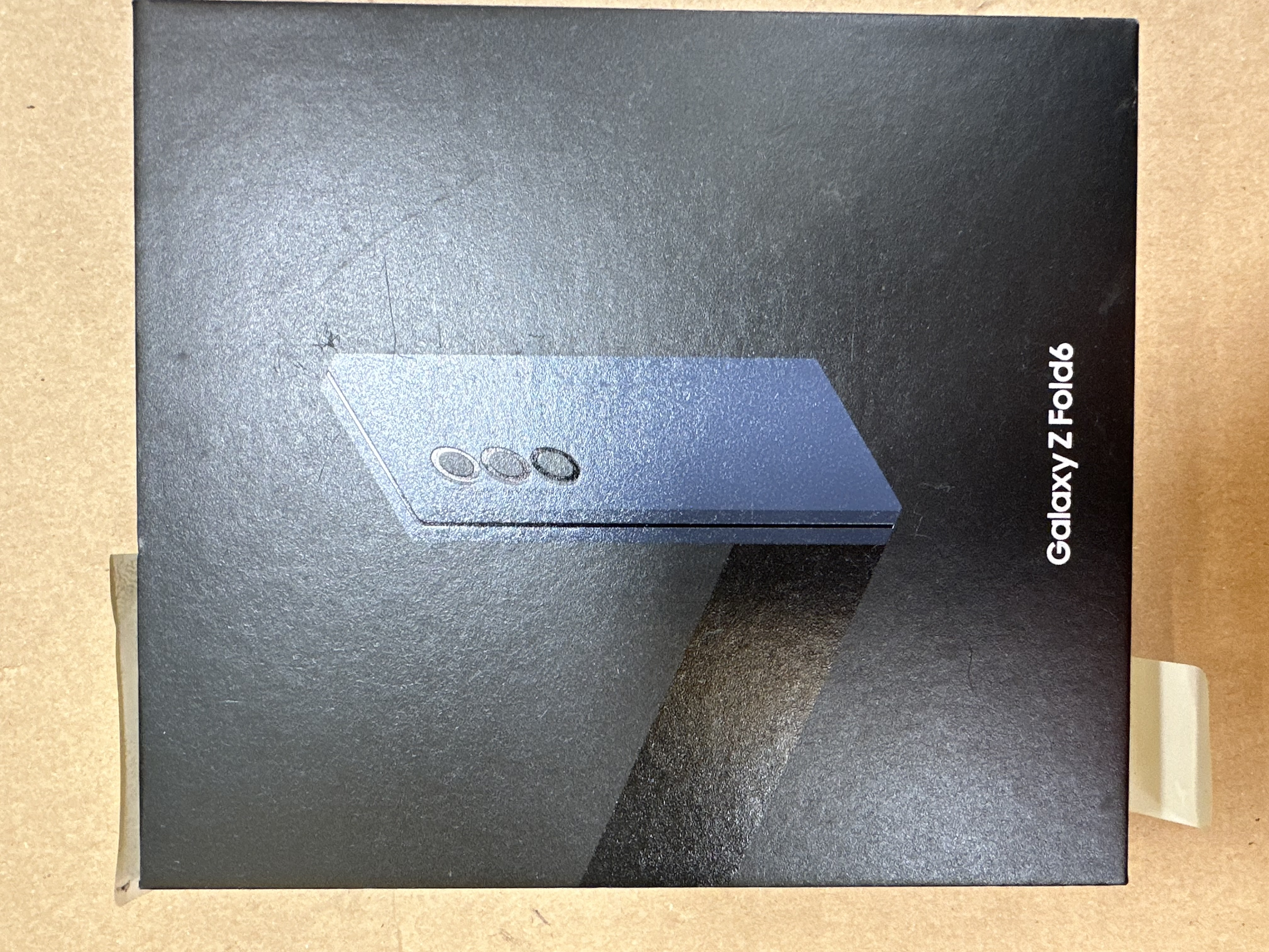 Częściowo otwarta skrzynka Galaxy Z Fold6, pokazująca niebieskie urządzenie na brązowej powierzchni.