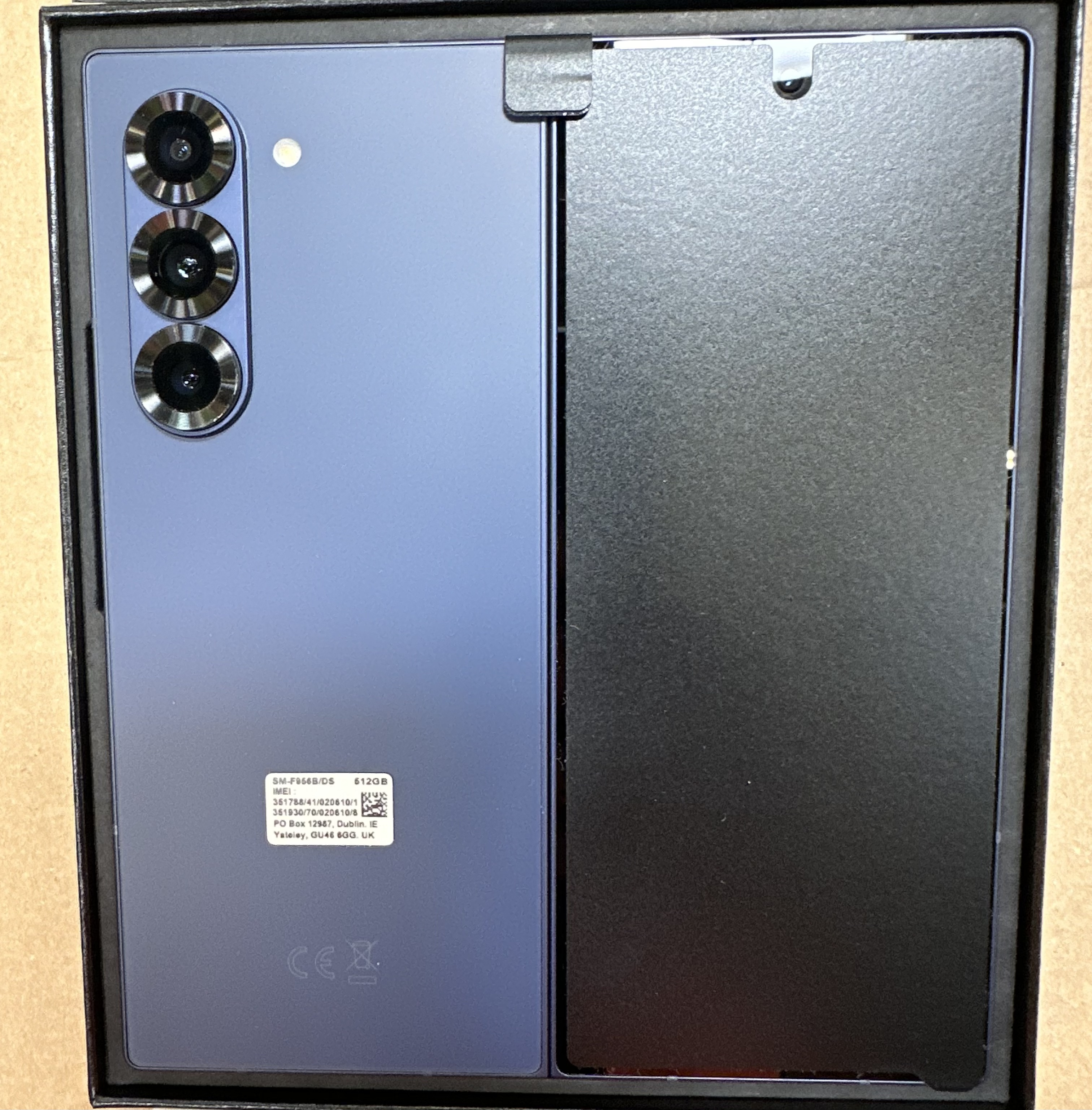 Niebieski smartfon z trzema aparatami w czarnym pudełku. Telefon jest otwarty.