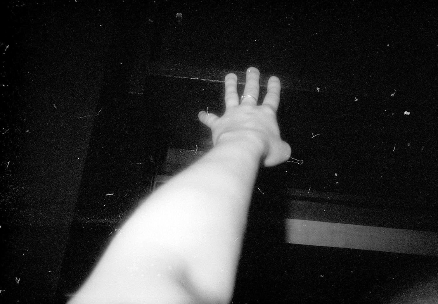 Die Hand einer Person, die nach oben greift, Finger ausgestreckt. Schwarzer Hintergrund.