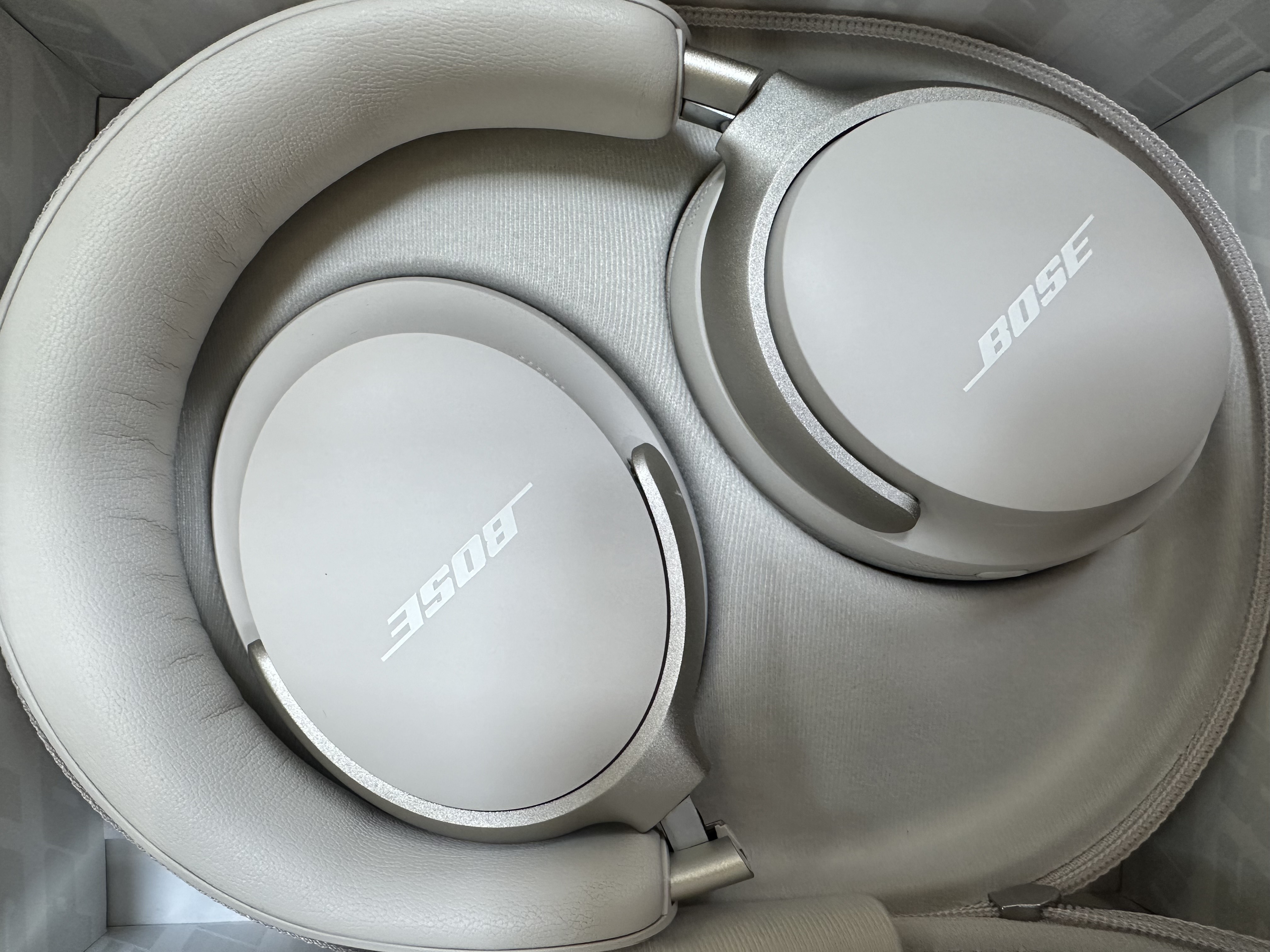 Białe słuchawki Bose w etui. Słuchawki i etui są jasnoszare. Logo Bose jest widoczne na nausznikach.