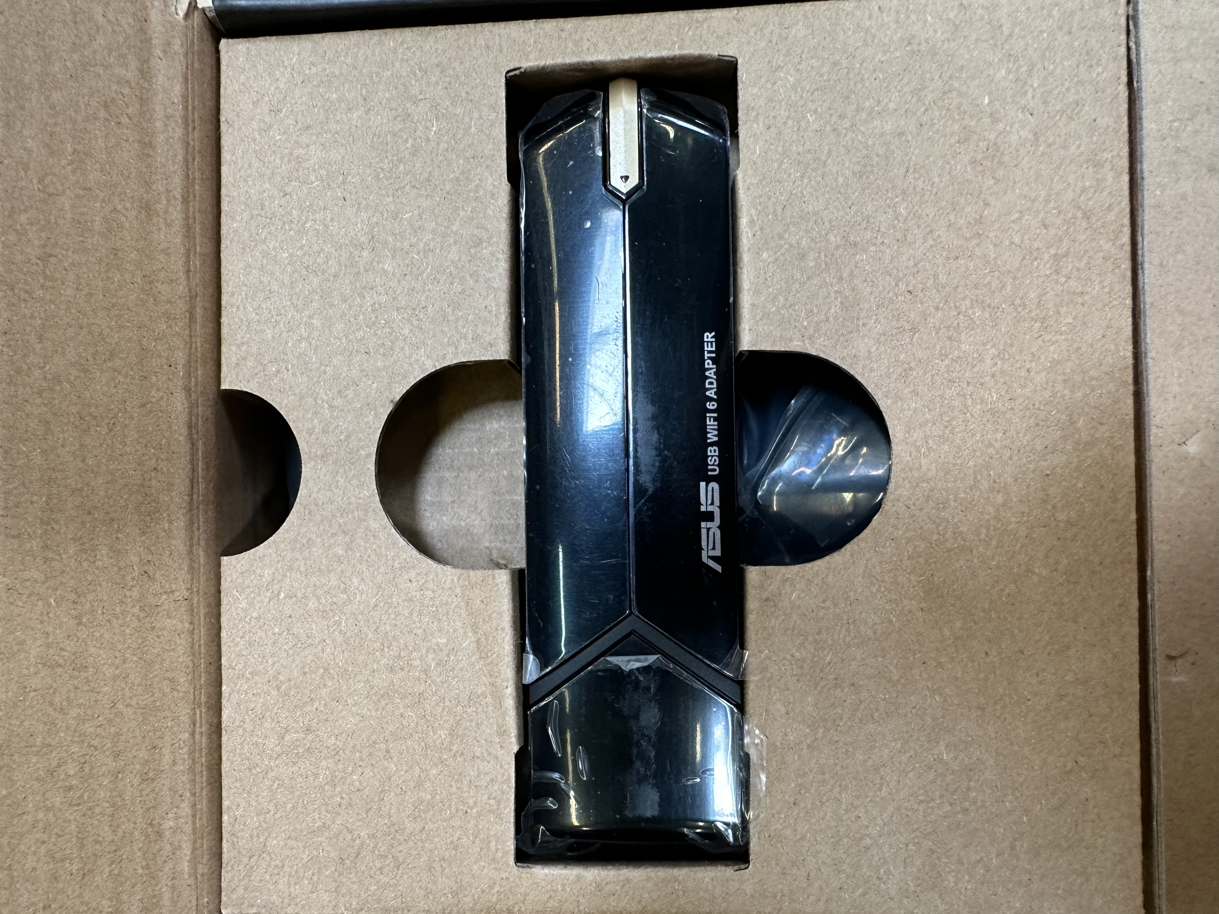 Czarny adapter ASUS USB WiFi 6 w kartonowym opakowaniu. Tekst na adapterze: ASUS USB WiFi 6 ADAPTER.