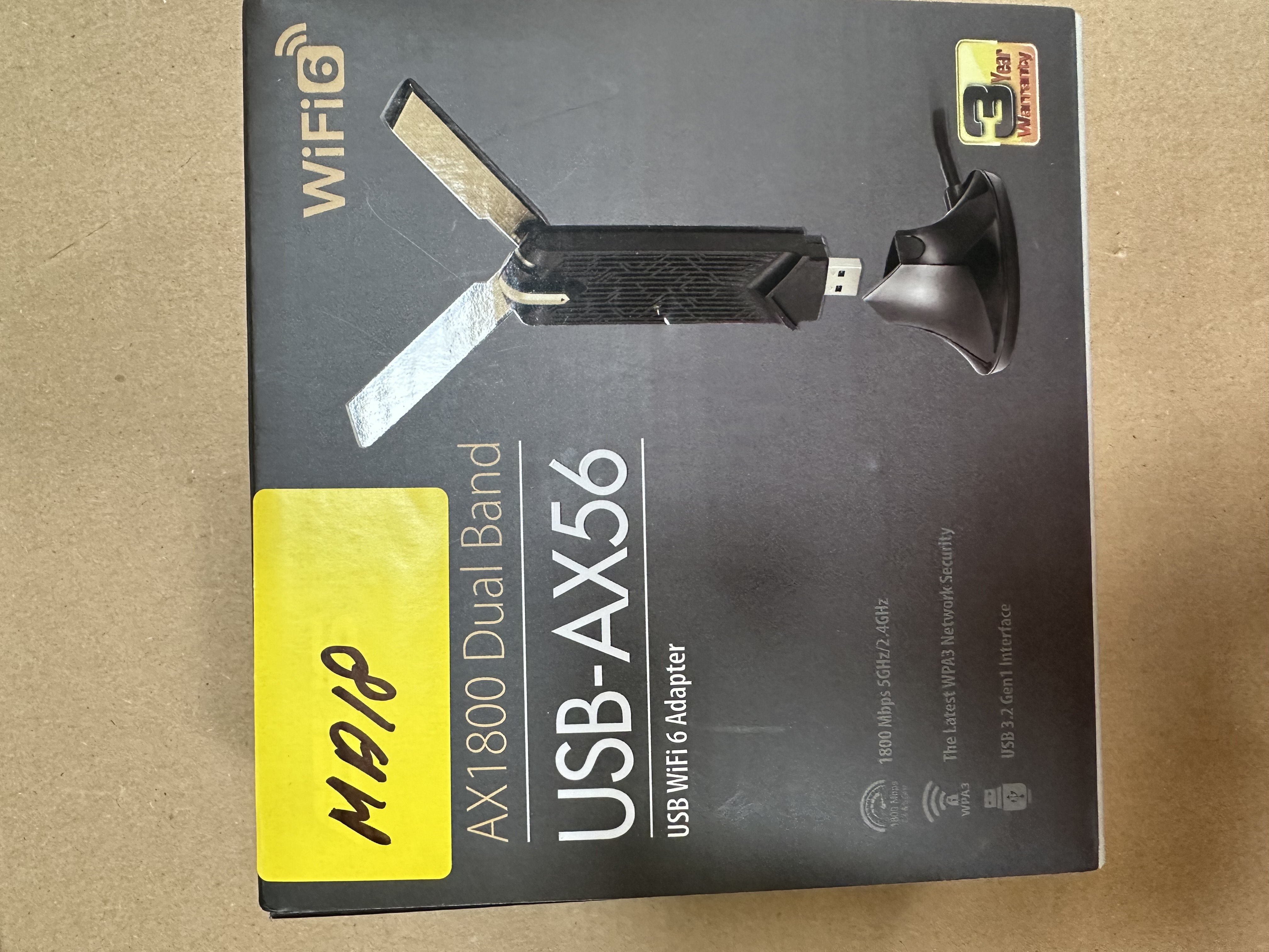 Pudełko z adapterem WiFi, model USB-AX56. Czarne pudełko z białym tekstem, żółta naklejka z czarnym tuszem.