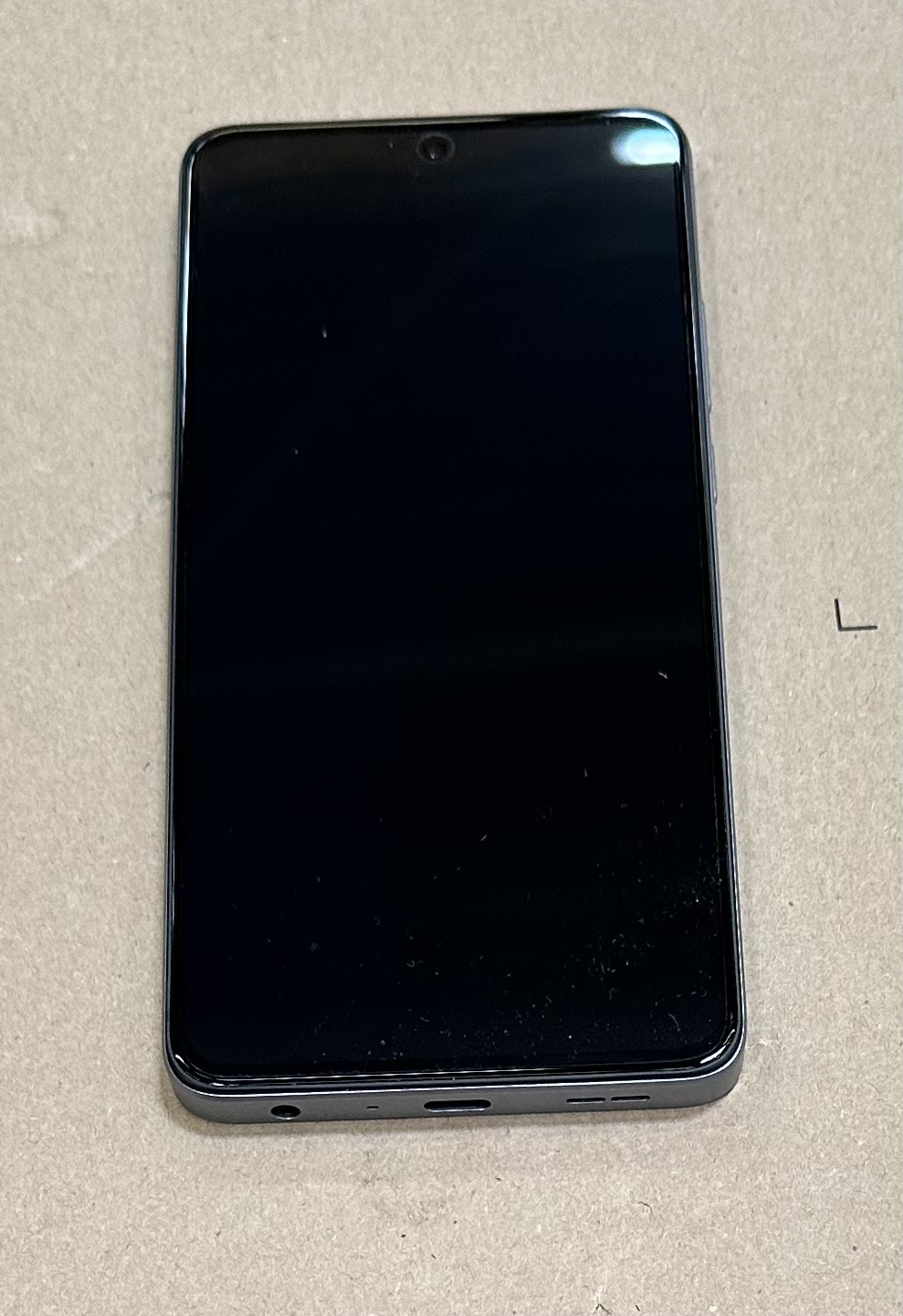 Czarny smartfon z czarnym ekranem na beżowej powierzchni. Na górze telefonu znajduje się aparat.