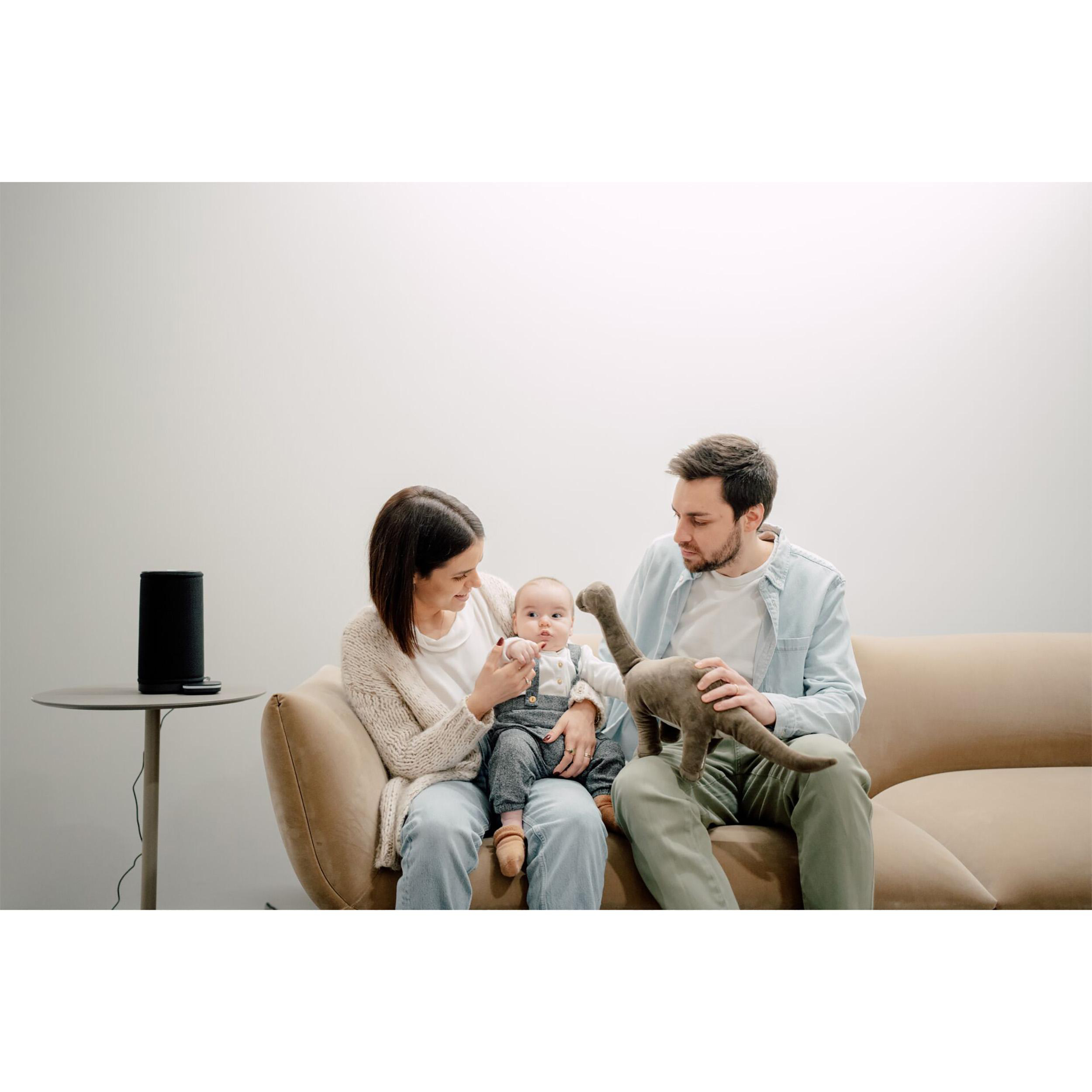 Eltern mit Baby auf dem Sofa, ein Lautsprecher an der Seite.