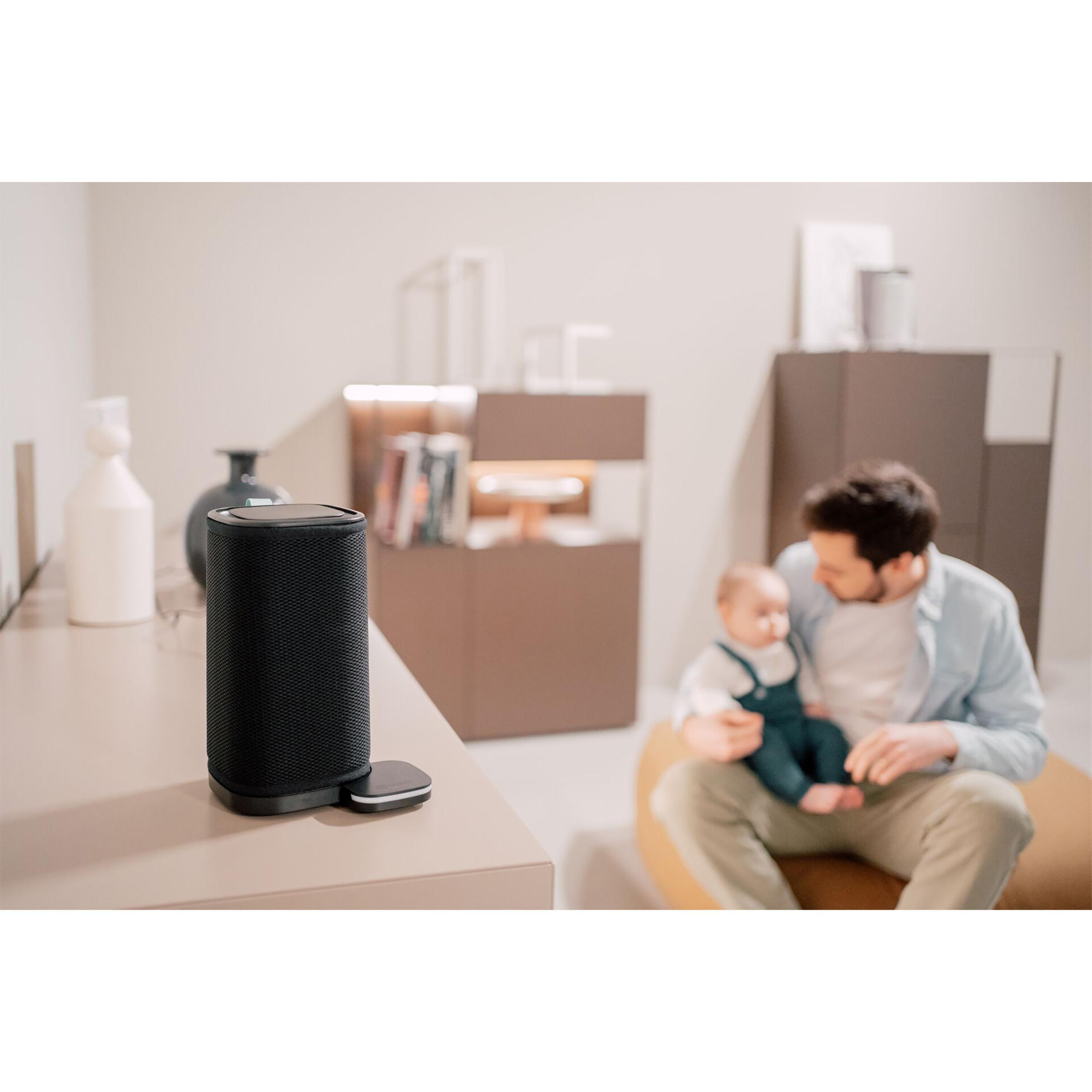 Schwarzer Lautsprecher auf einem Tisch, Mann mit Baby im Hintergrund.